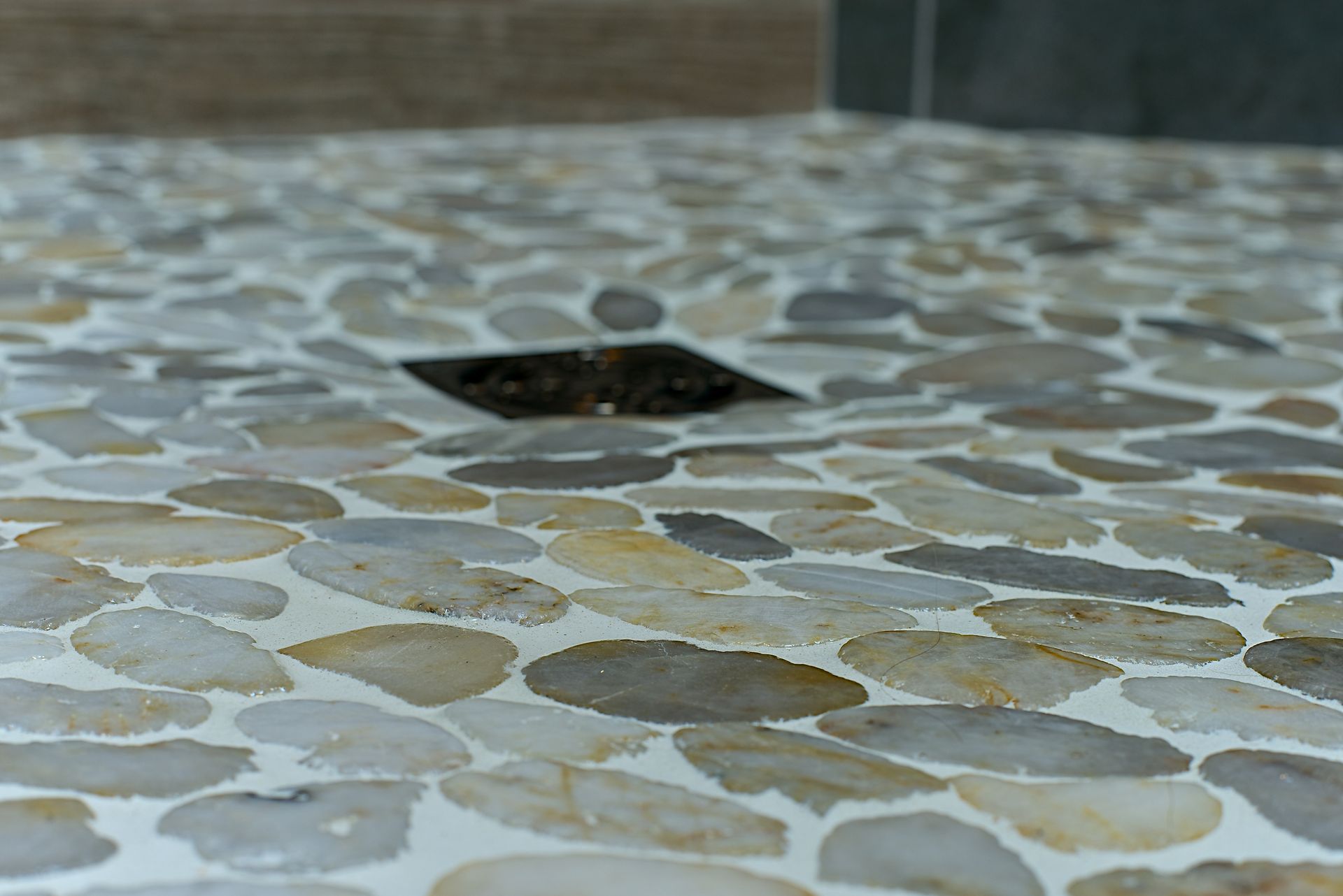 Close-up of a shower floor with a pebble tile design, featuring a square drain in the center.