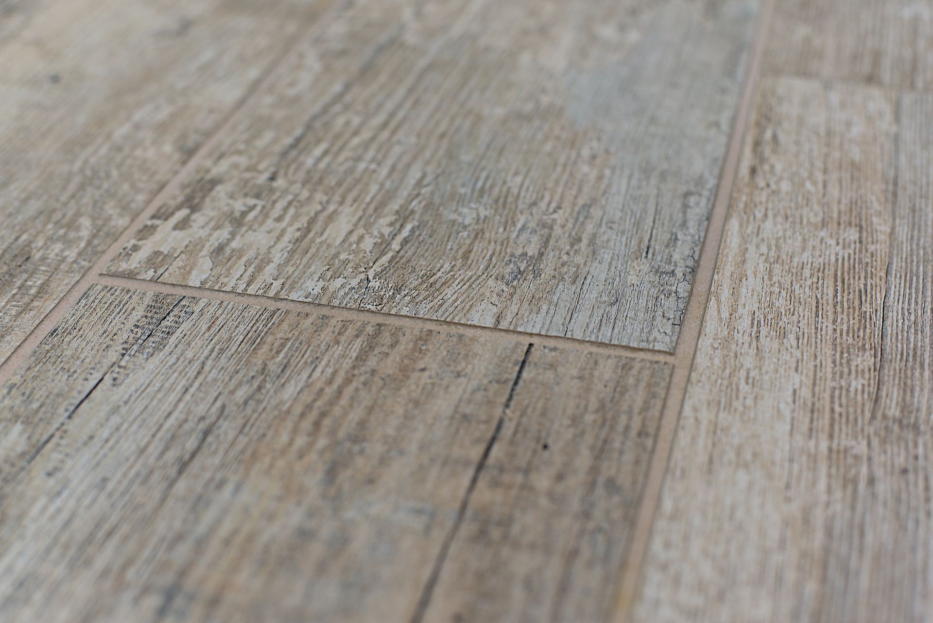 Wood-look floor tiles, light brown with dark grain, in a close-up, angled view.