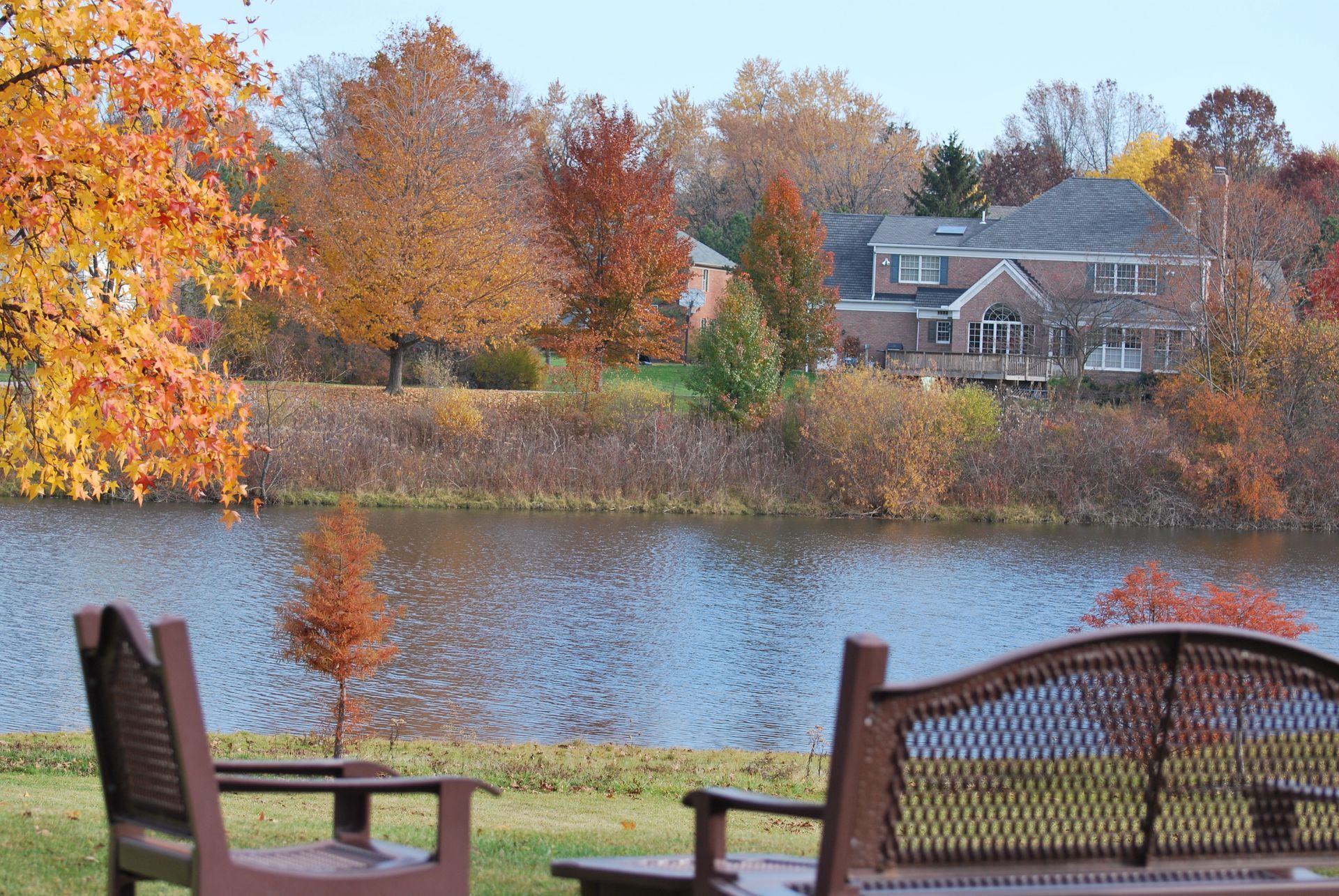 A couple of chairs sitting next to a lake with a house in the background