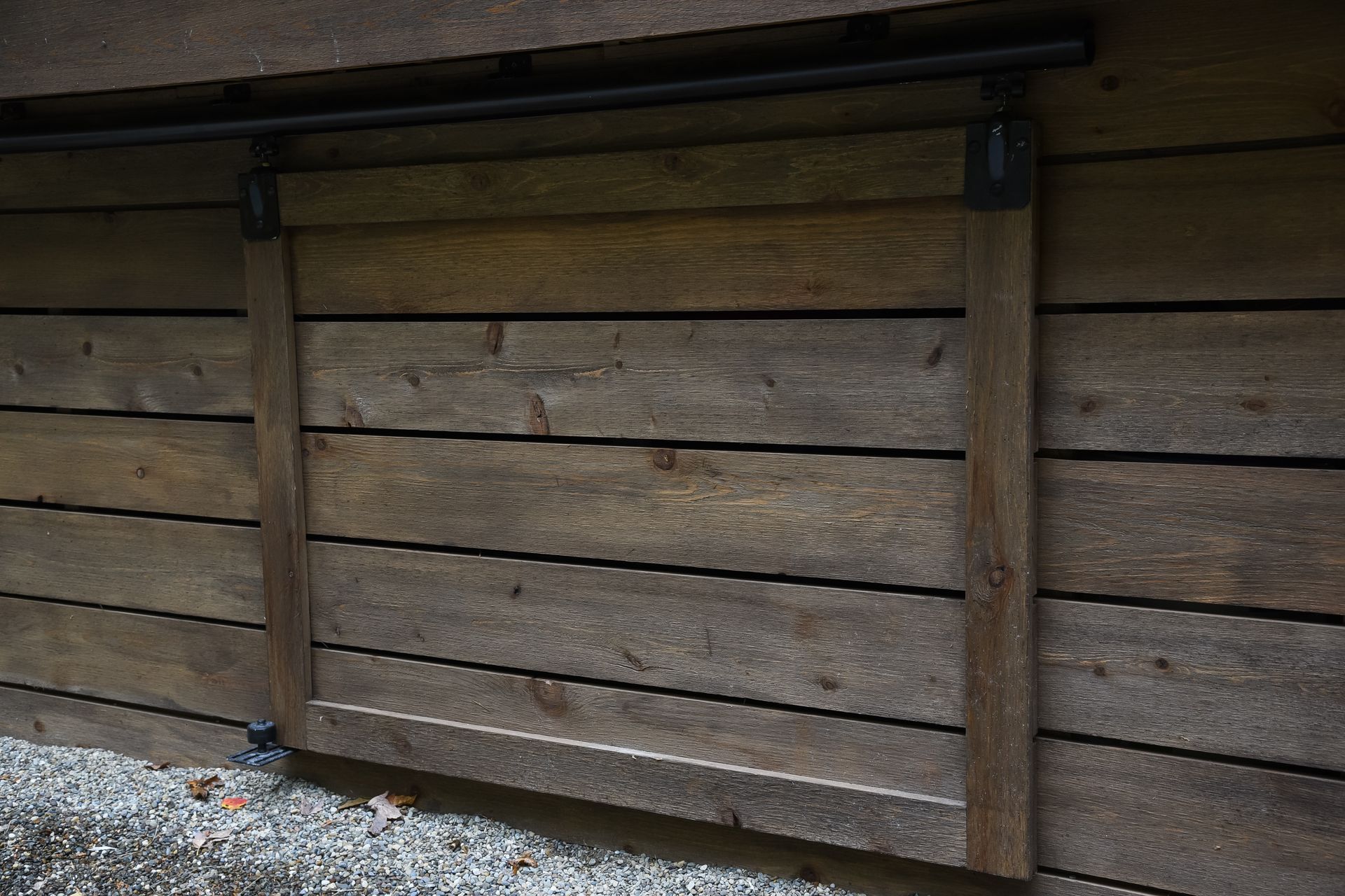 Wooden sliding barn door on a wood wall. Black track and hardware. Exterior setting.