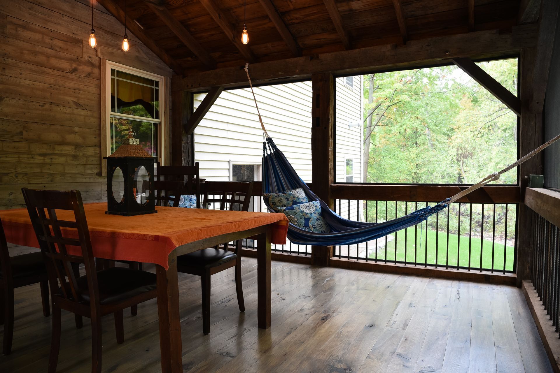 Cozy screened porch with a dining table, hammock, and wooden walls.