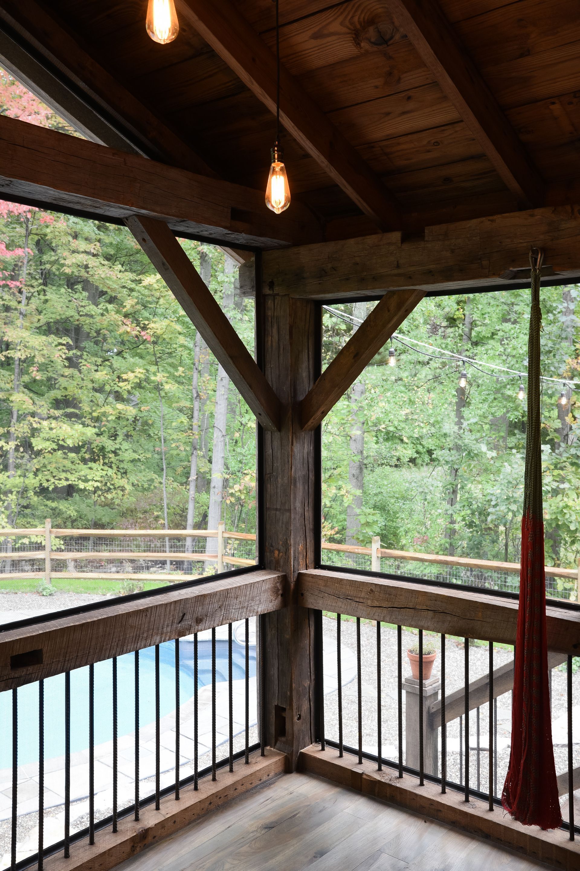 Wooden screened porch overlooking a pool and trees with hanging lights.