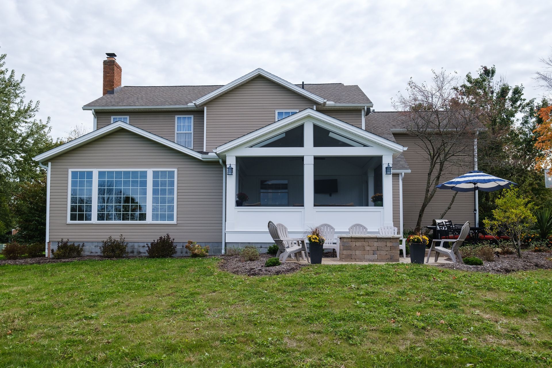 Back of a house with a screened-in porch, a fire pit, and an umbrella on a lawn.