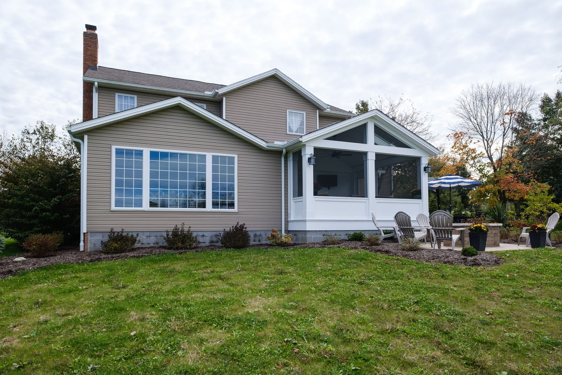 Tan house with a screened porch, large windows, and green lawn under a cloudy sky.