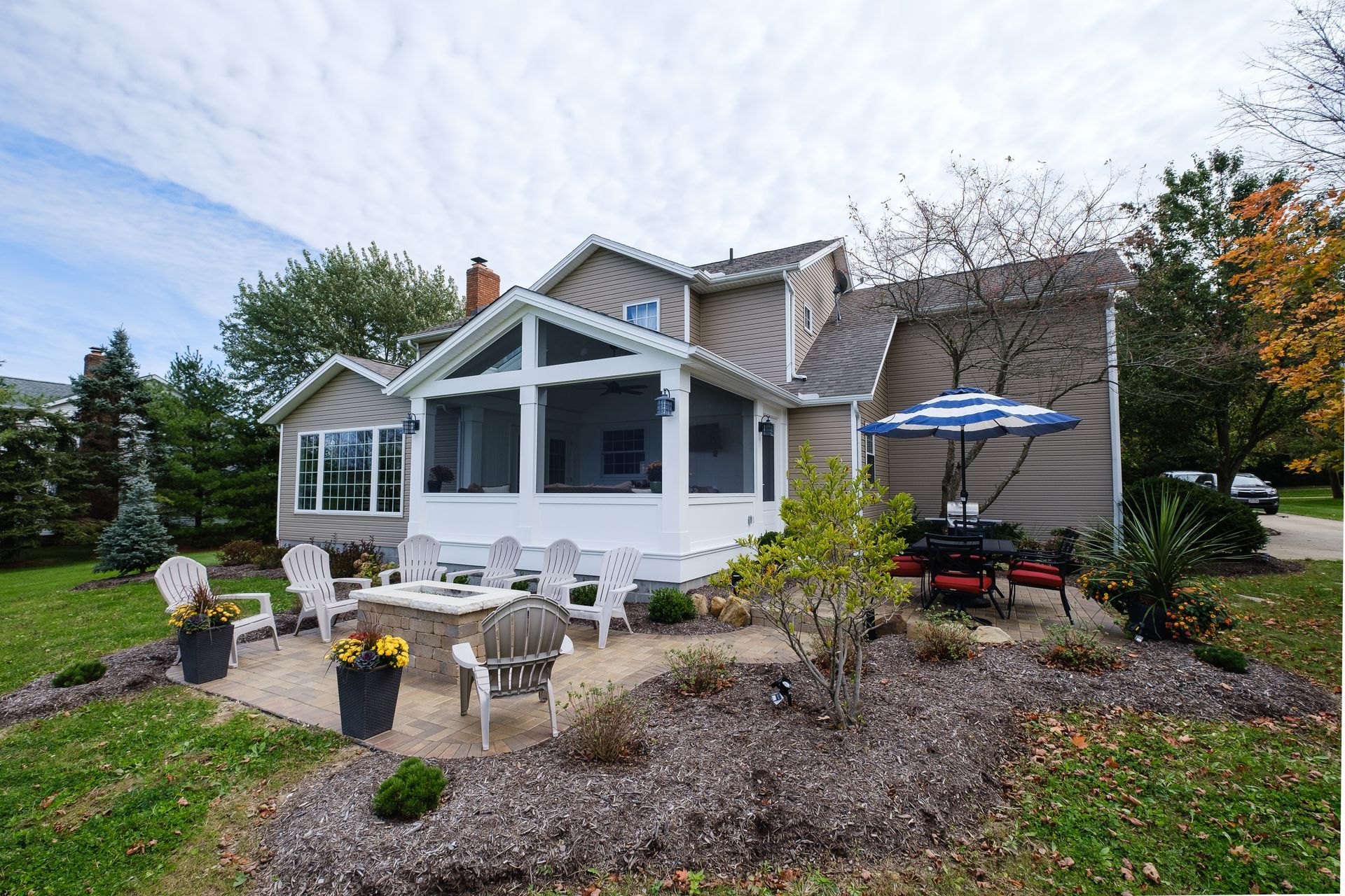 House exterior with a patio and screened porch. Chairs surround a fire pit, table has umbrella.
