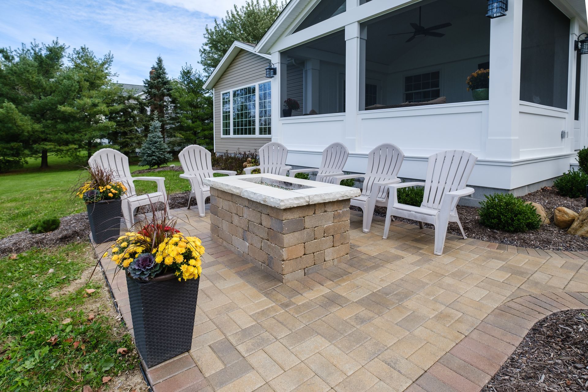 Patio with fire pit, Adirondack chairs, potted flowers, and screened porch.