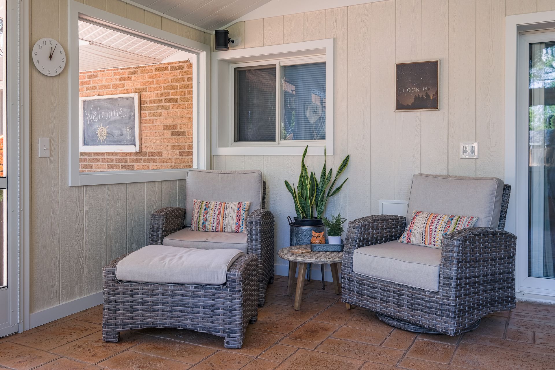 Outdoor seating area with two wicker chairs, ottoman, small table, and potted plants.