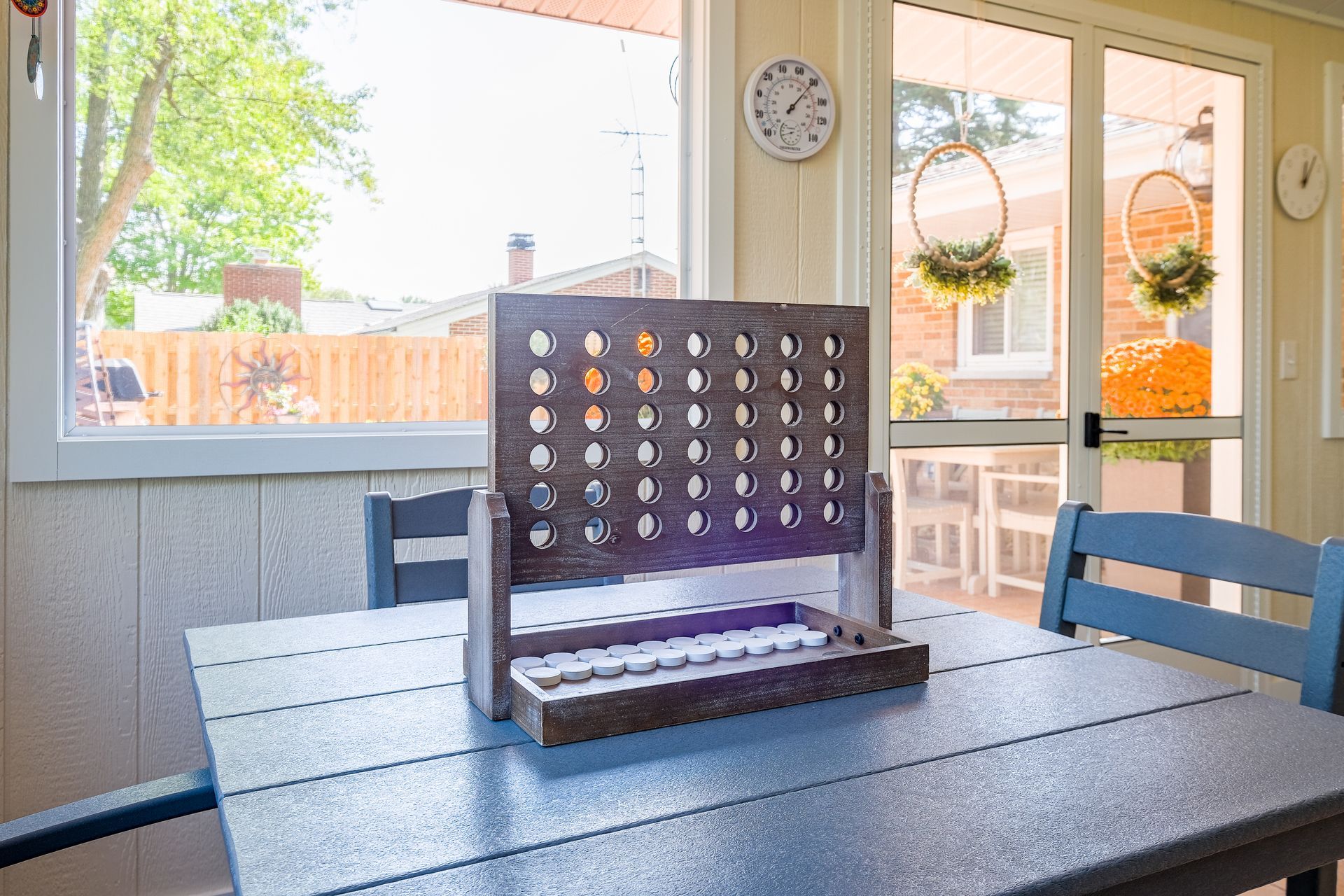 Connect Four game on a blue table near a window, with a view of a backyard.