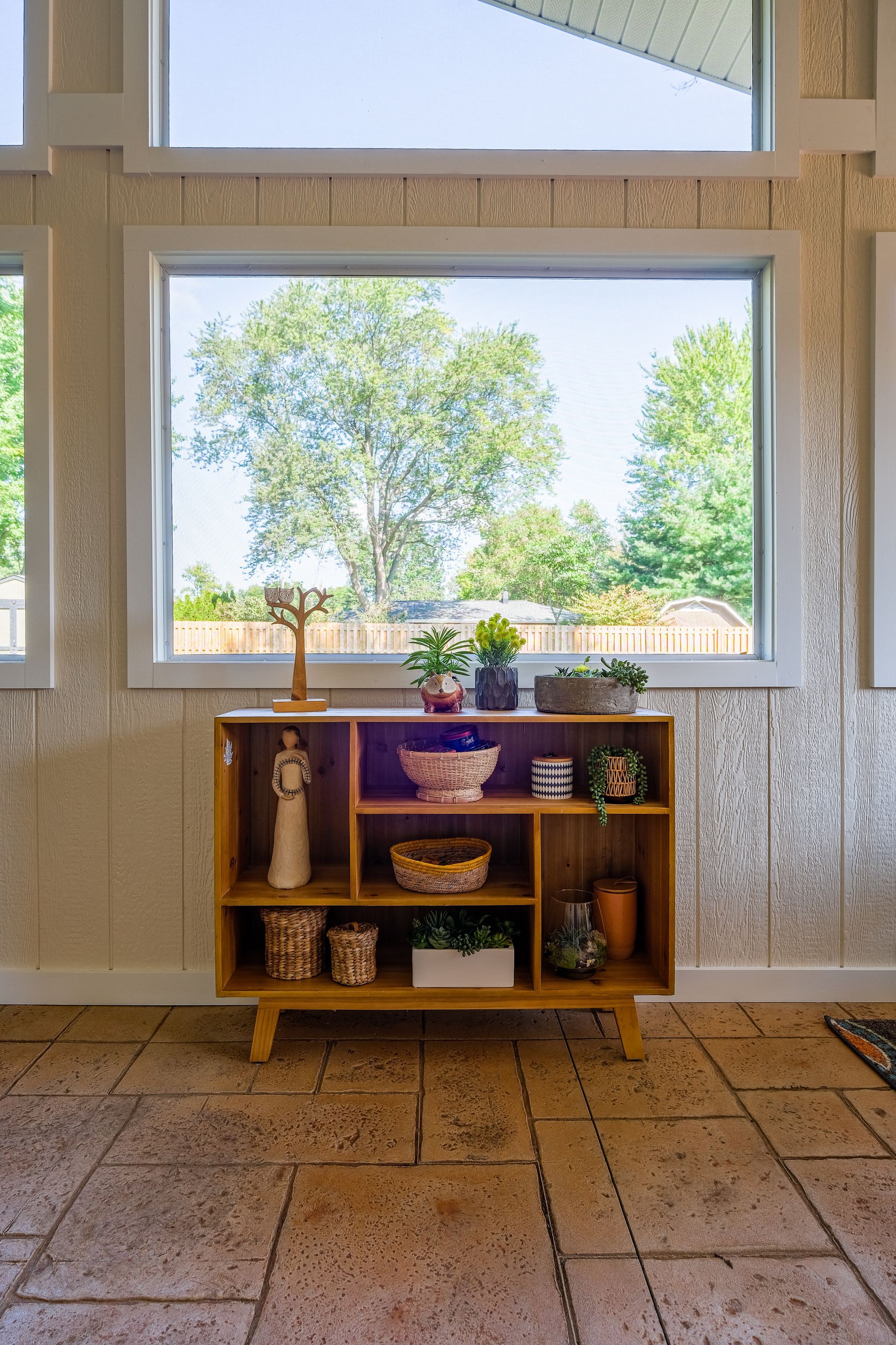 Wooden shelf with decor in front of a large window overlooking trees.