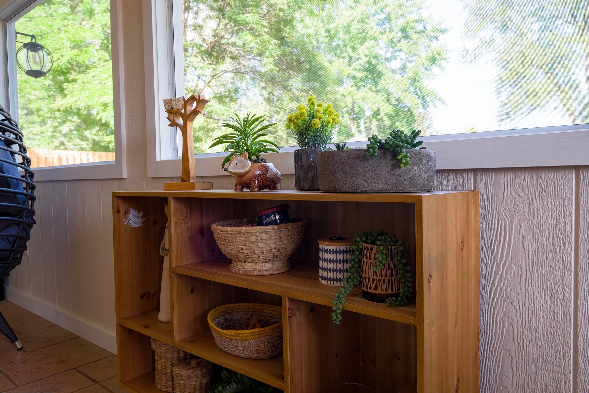 Wooden shelf with plants and decor against a window overlooking greenery.
