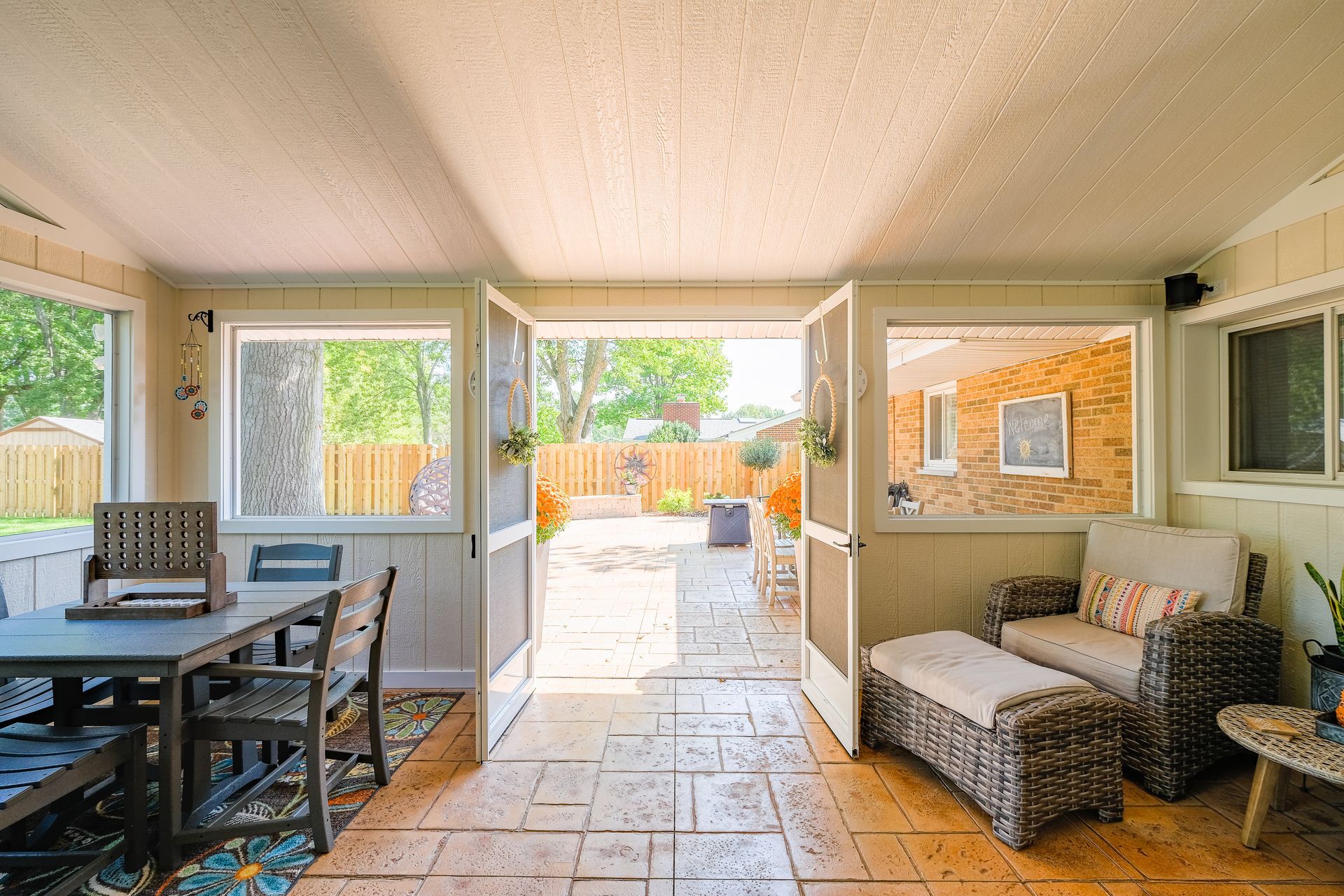 Sunroom with open doors to a backyard; table and chairs on the left, wicker seating on the right.