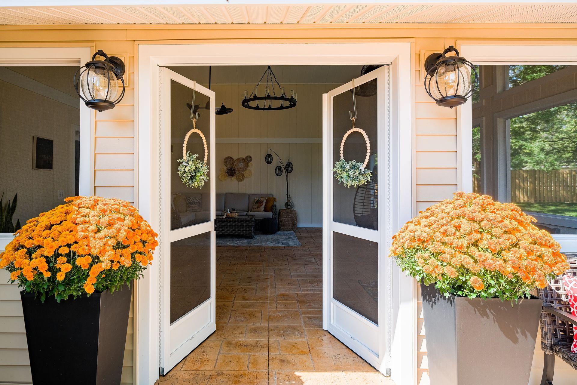 Open double doors of a home, flanked by orange mums in black and gray pots.