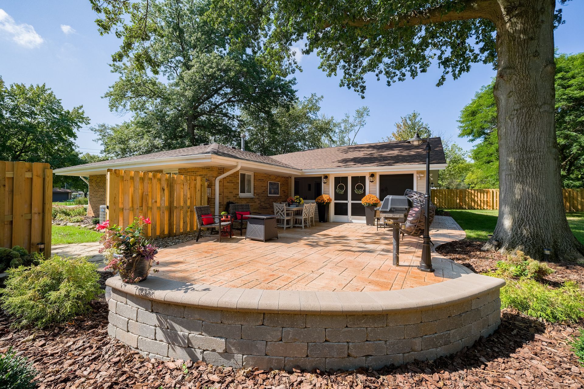 Backyard patio with brick retaining wall, grill, and seating under a covered area.