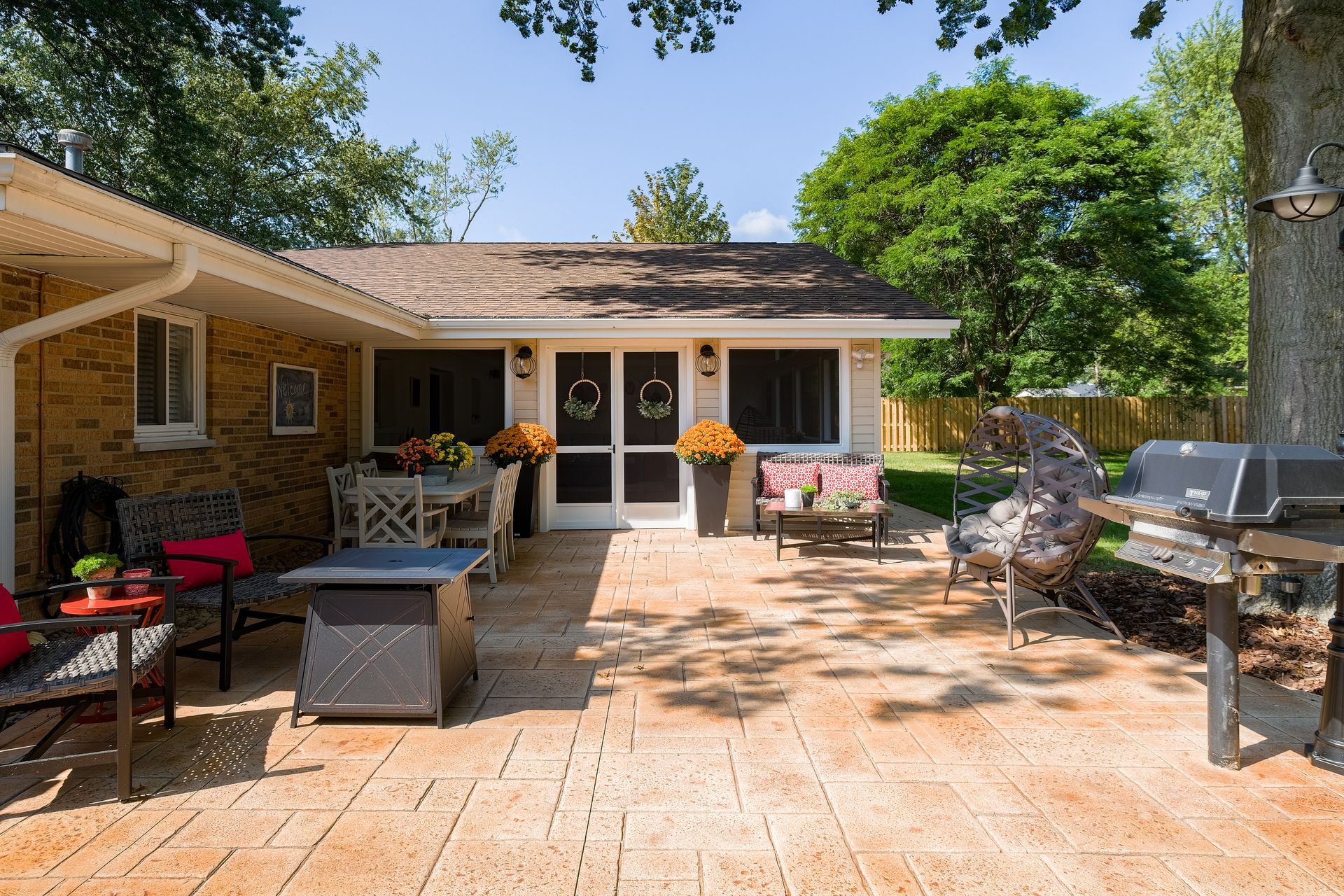 Backyard patio with dining and lounge areas, grill, and a small building with double doors.