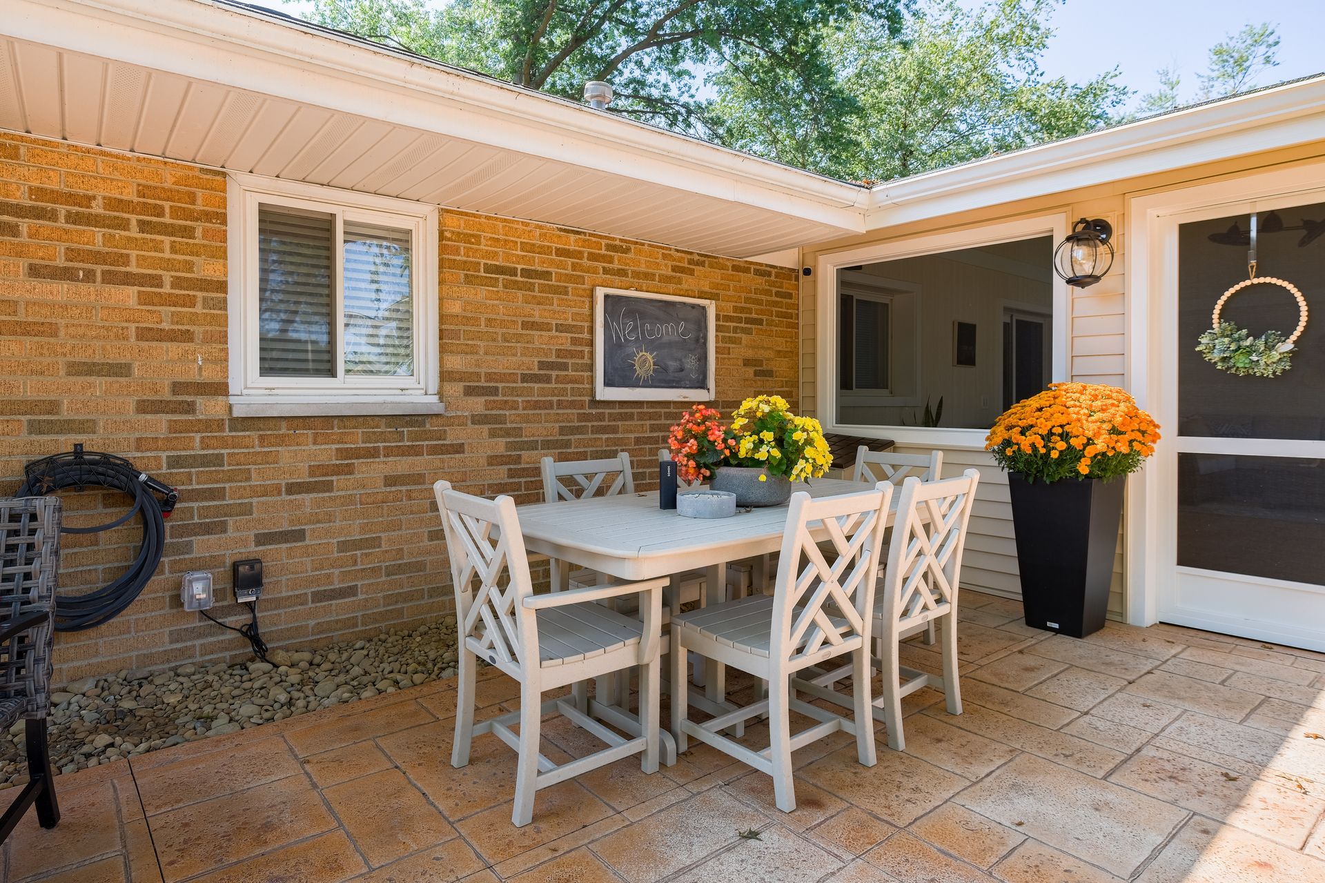 Patio with white table and chairs, brick wall, potted mums, and open doorway.