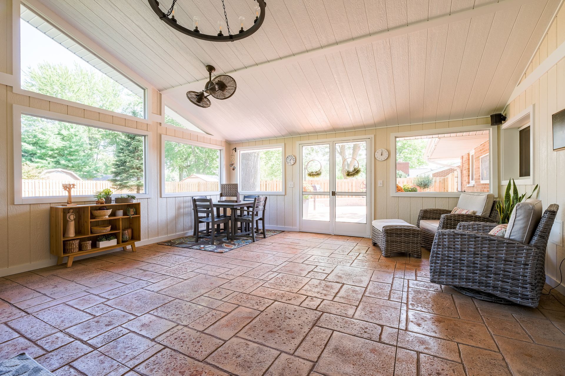 Sunroom with brick floor, large windows, dining table, and wicker seating.