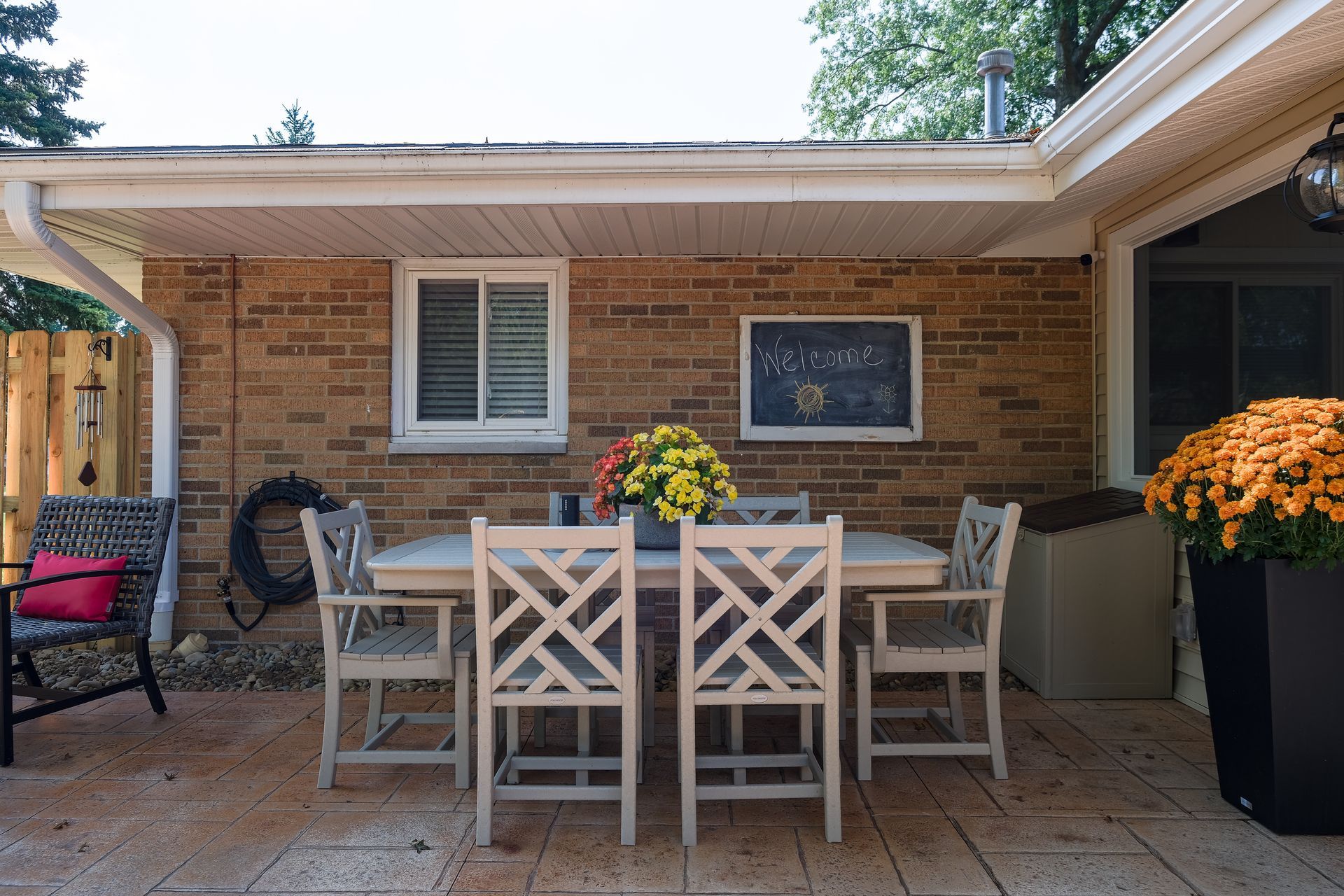 Patio with a table and chairs, brick wall, flower pots, and a chalkboard.