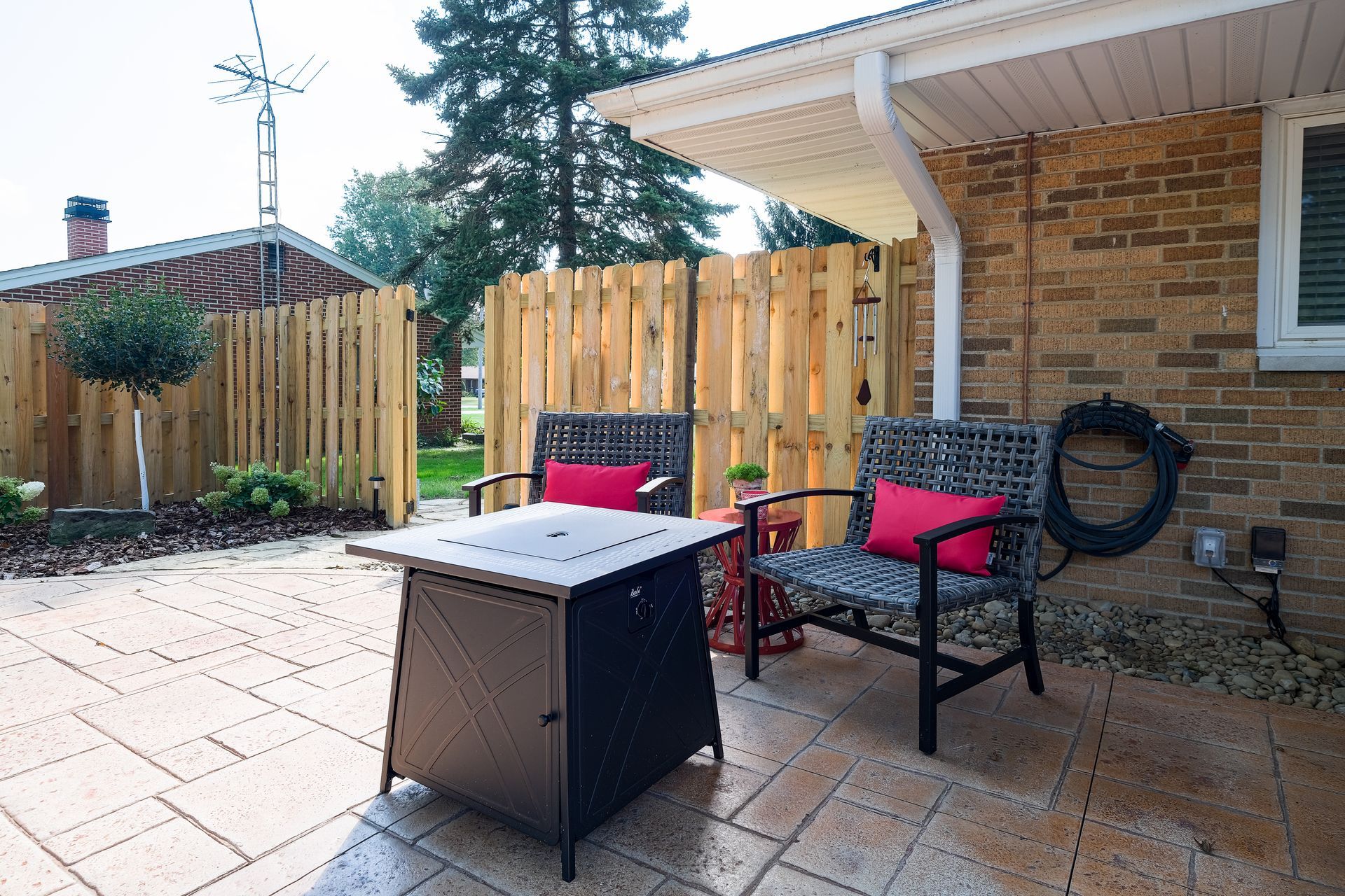 Patio with seating, fire pit, and wooden fence. Brick house exterior.