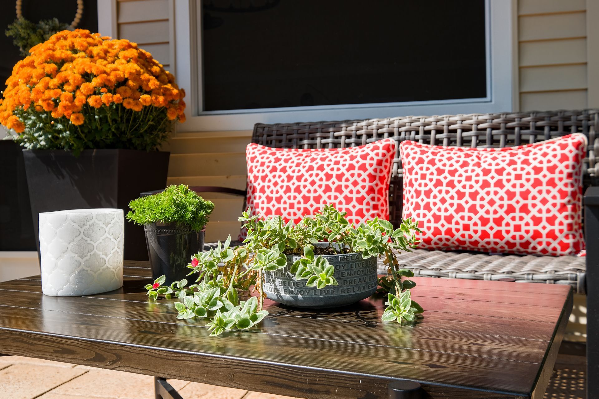 Outdoor patio with fall decor: orange mums, red patterned pillows, plants on a black table.