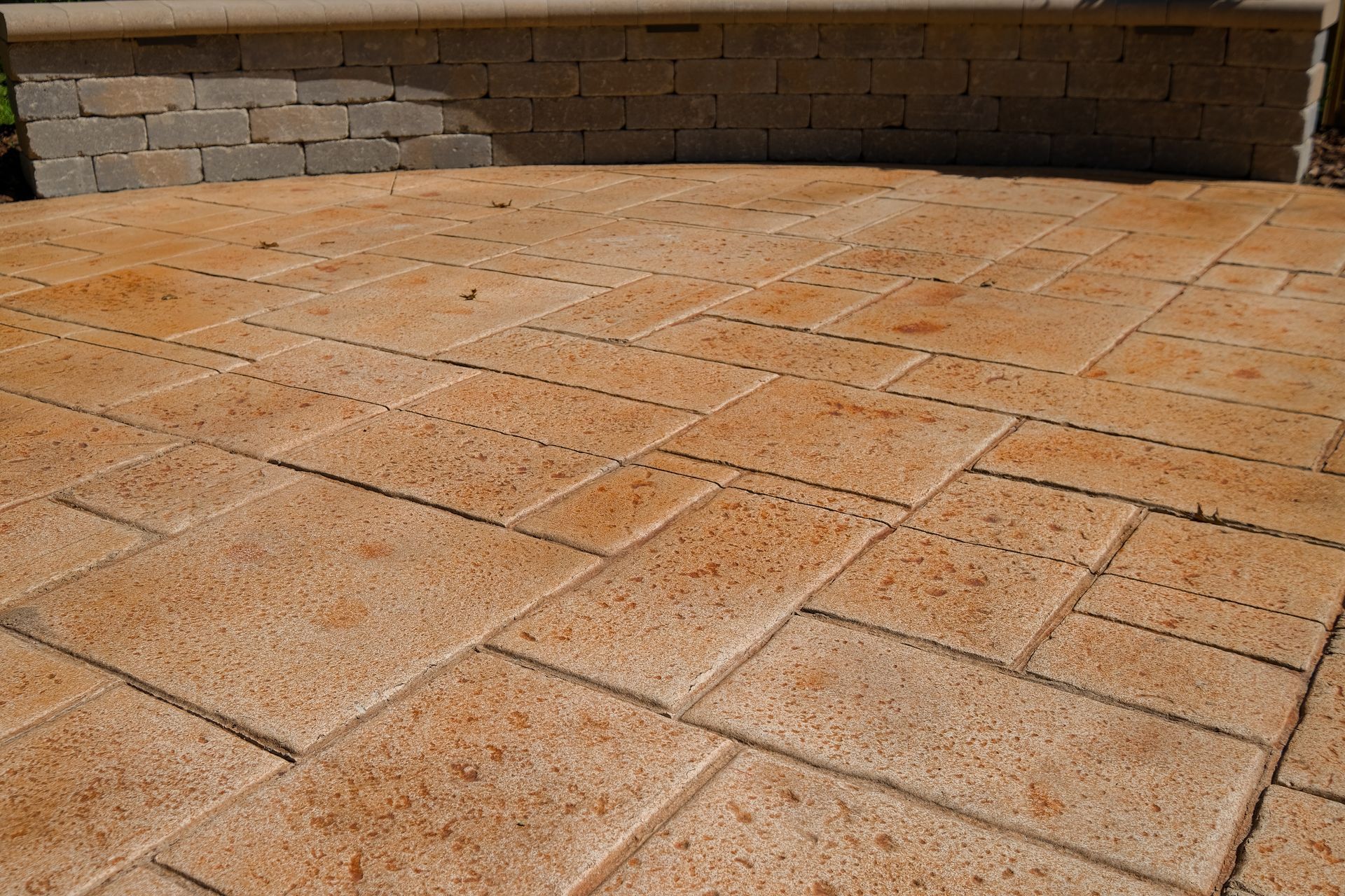 Stone patio with light brown paving stones and a low brick wall.
