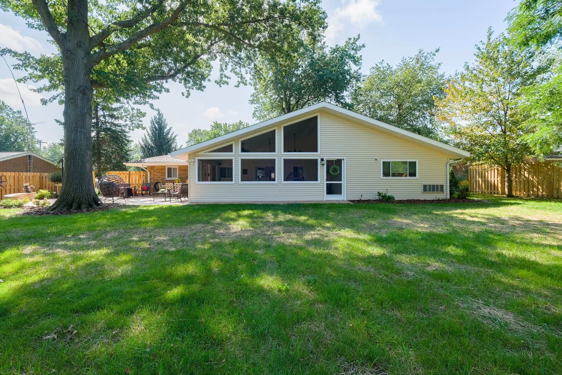 Backyard view of a beige house with a screened-in porch, green lawn, and trees.