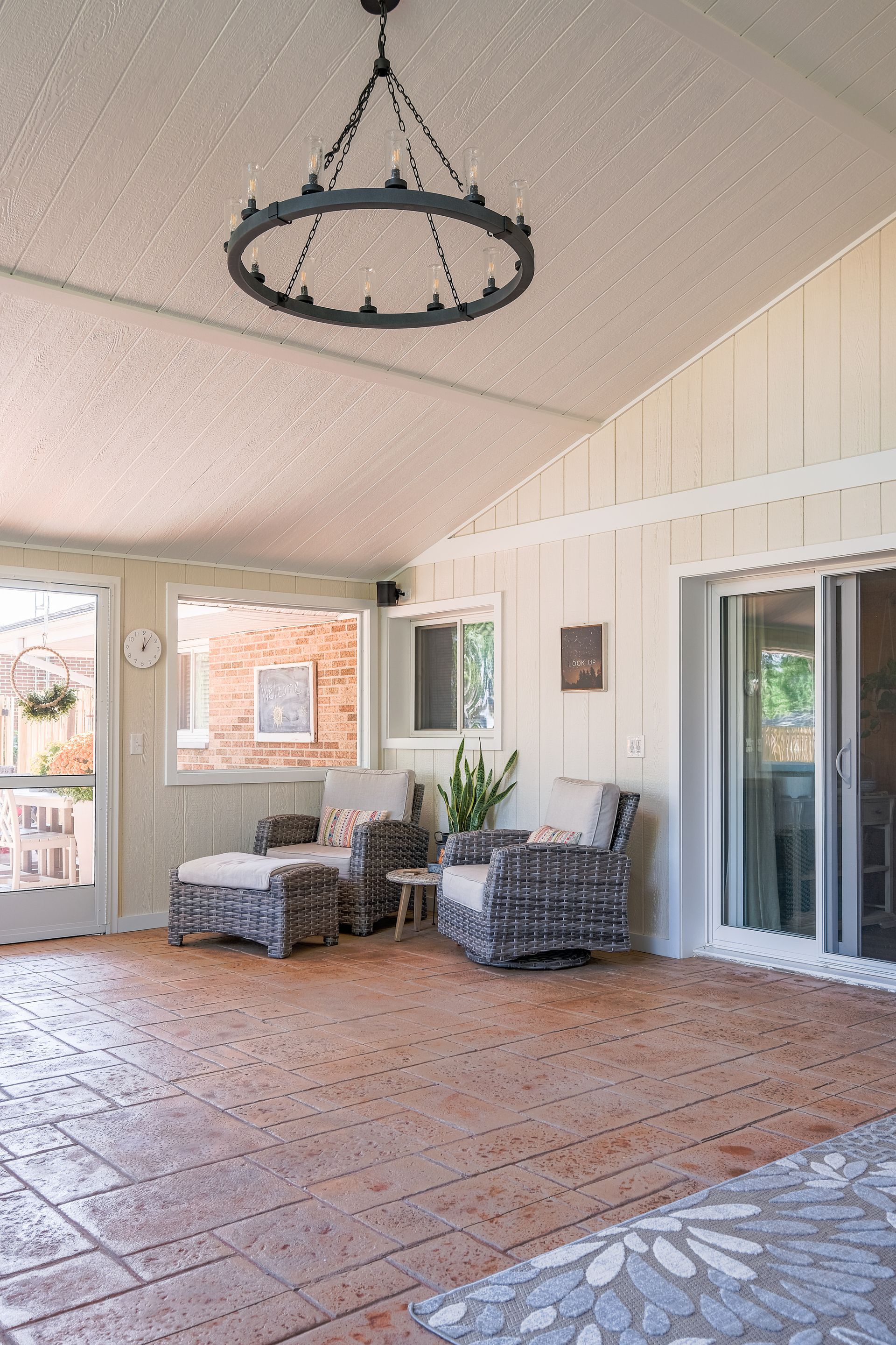 Sunroom with brick floor, wicker furniture, and a large chandelier.