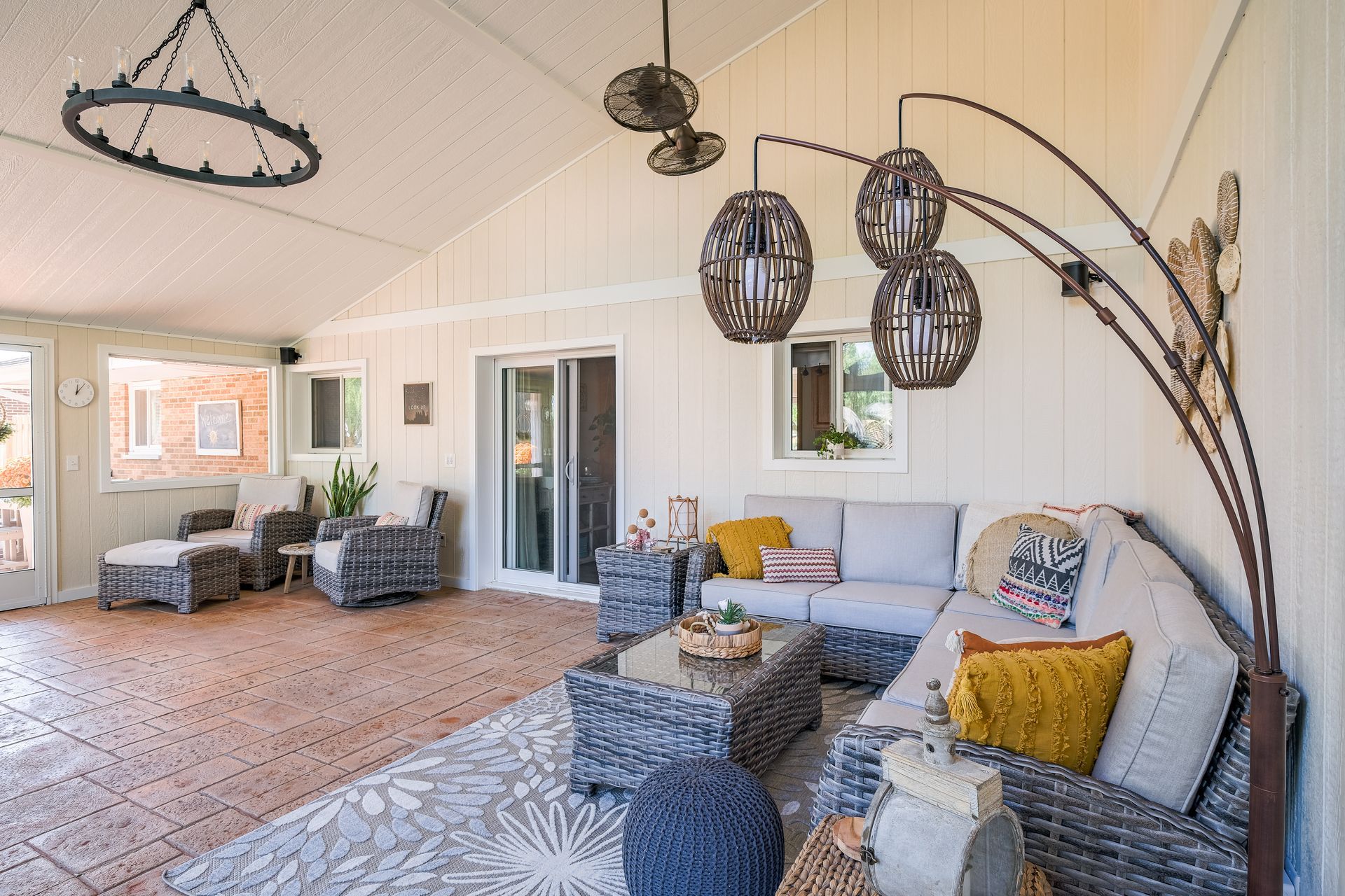 Outdoor living space with gray wicker furniture, area rug, and hanging lights.