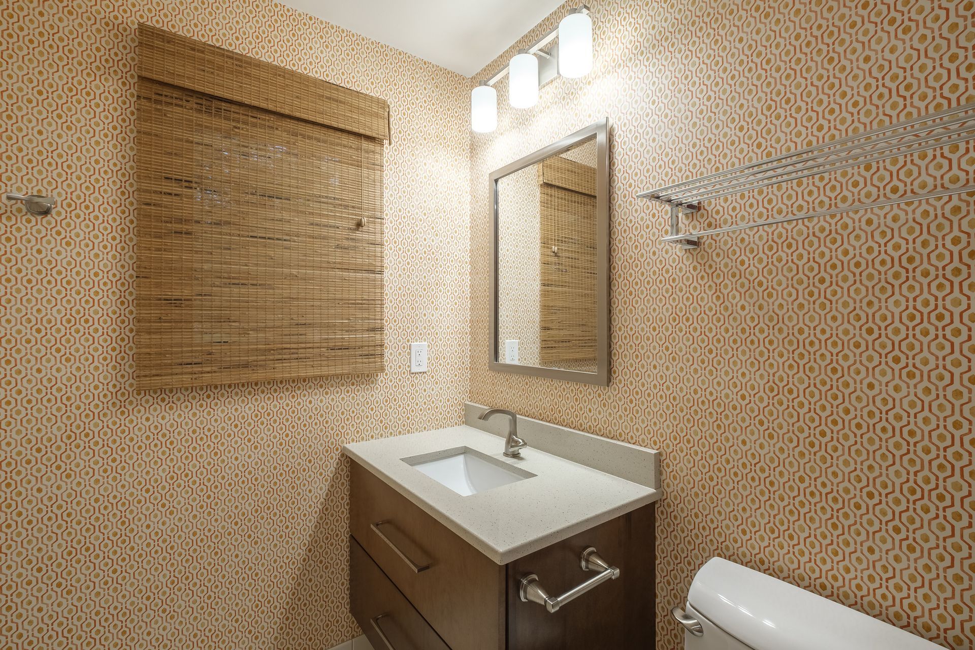 Small bathroom with patterned wallpaper, vanity, mirror, and toilet.