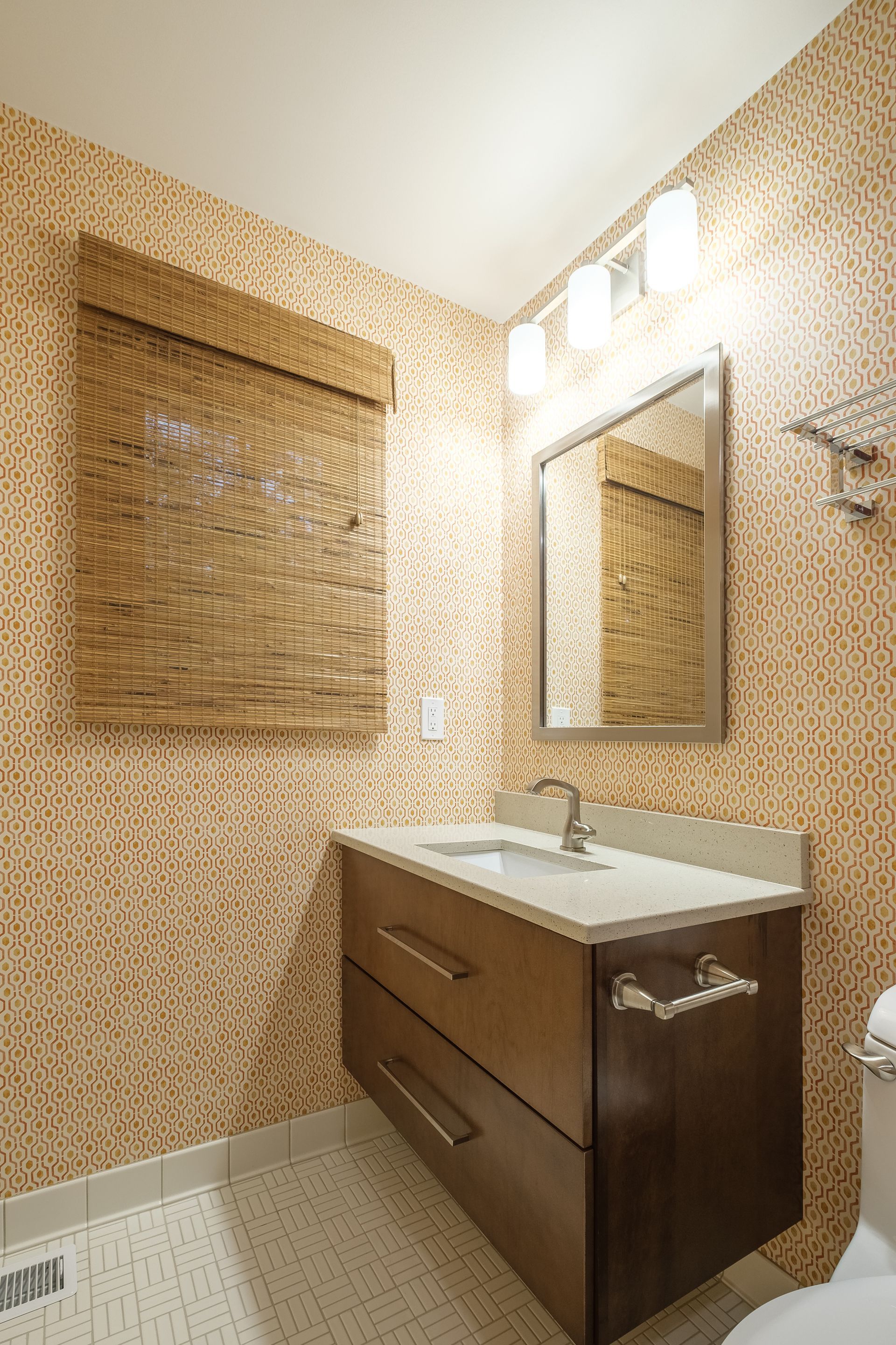 Bathroom with a wooden vanity, mirror, and textured wallpaper.