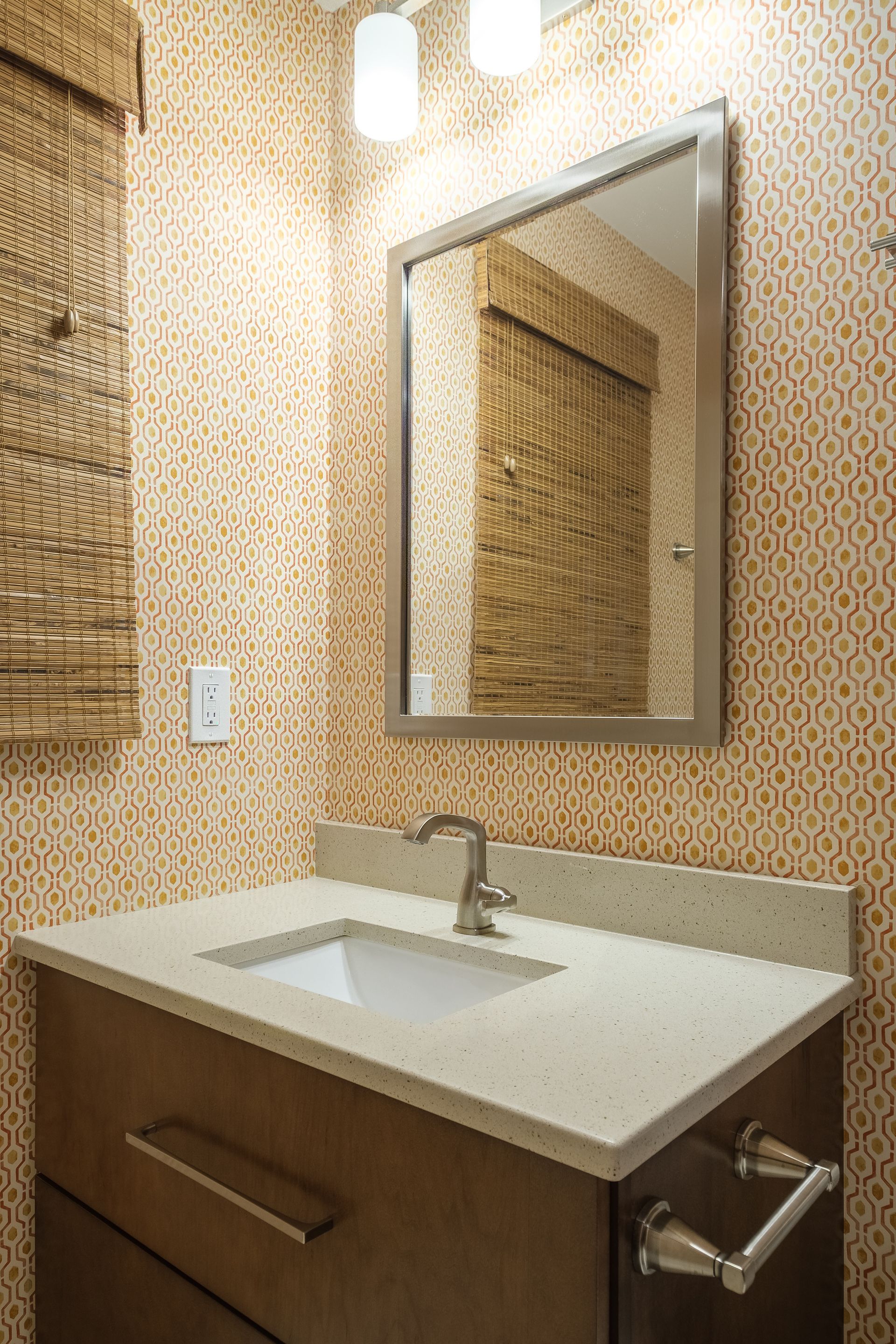 Bathroom with vanity, mirror, patterned wallpaper, and woven blinds.