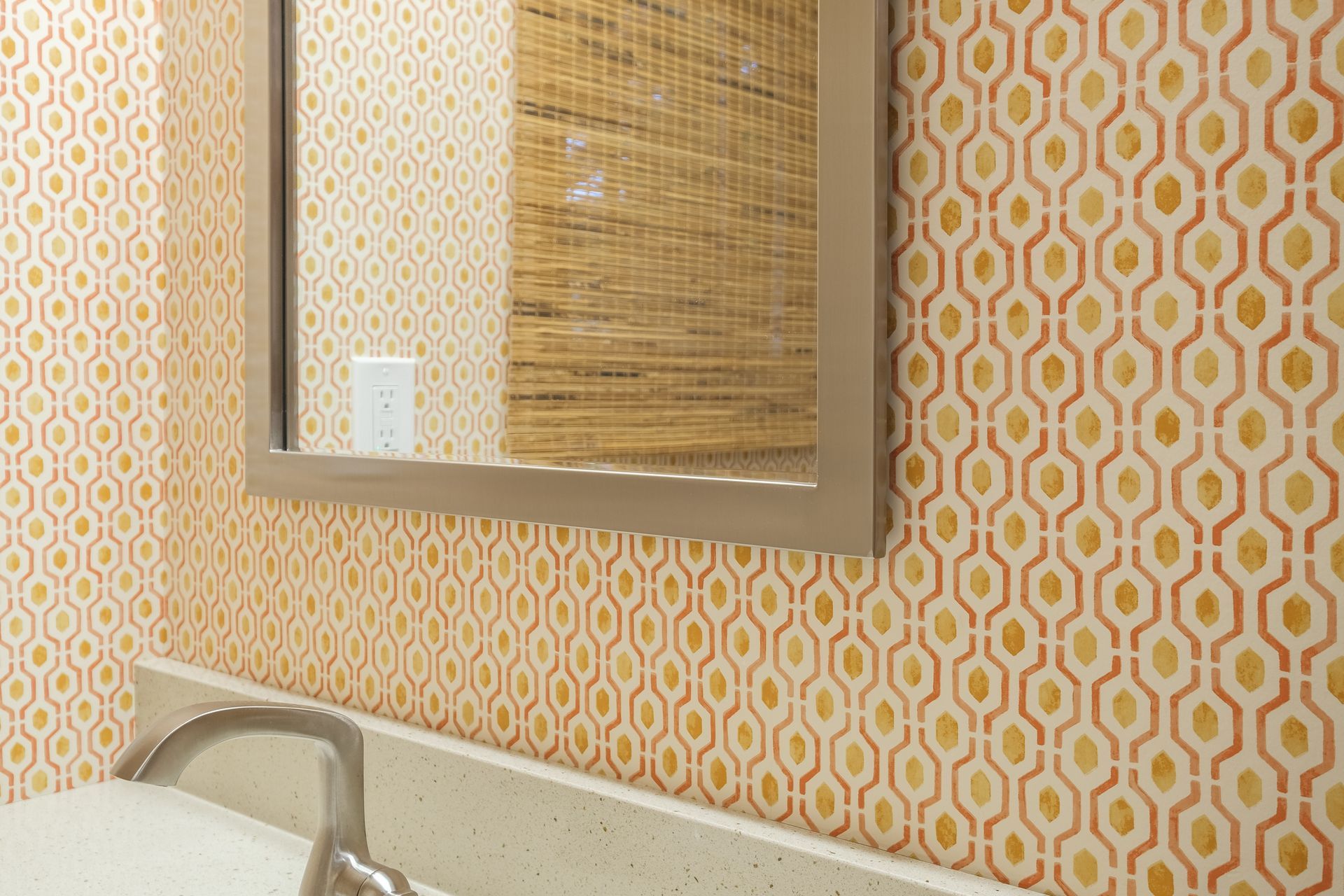 Bathroom with patterned orange wallpaper, a mirror, and a sink.