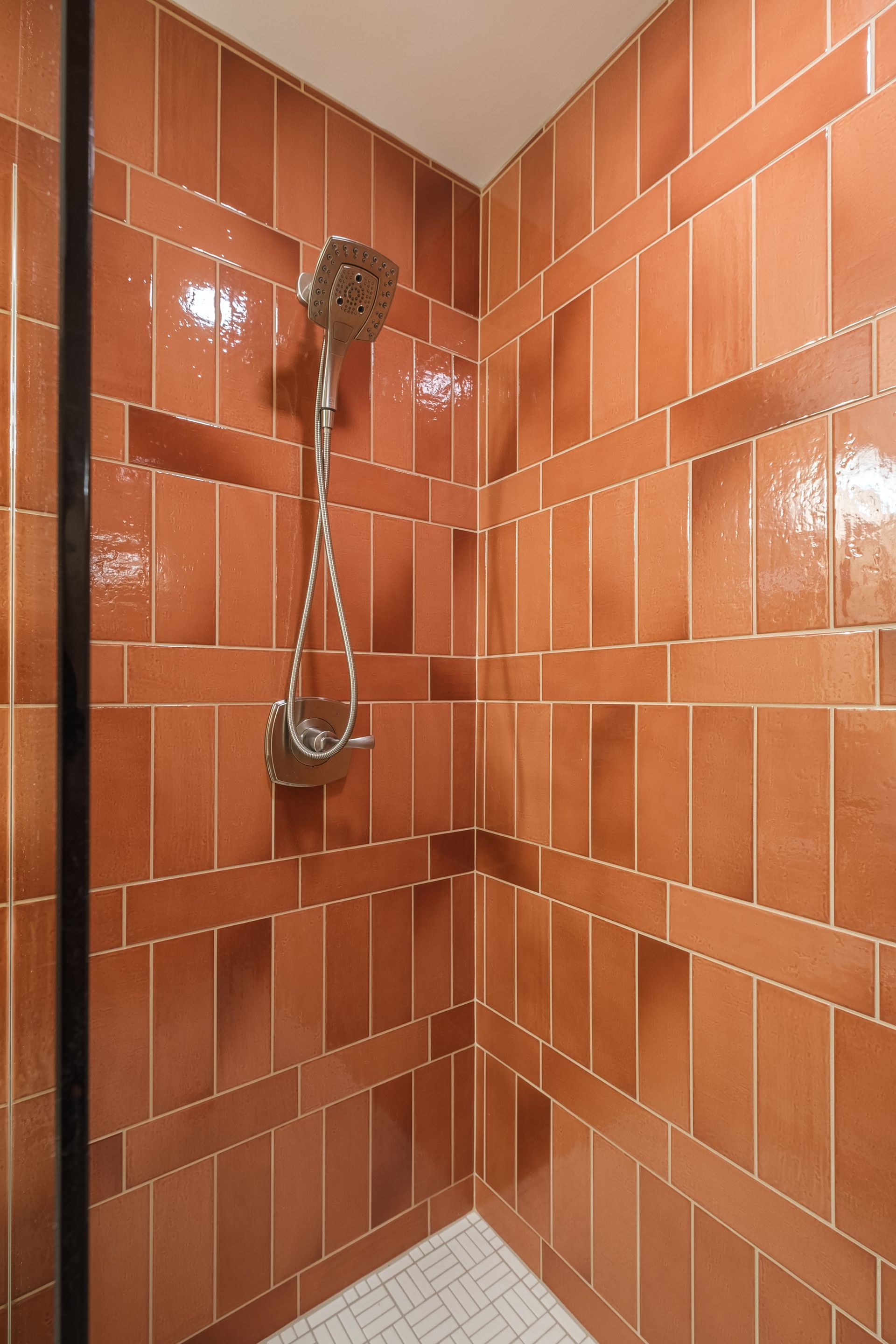 Shower with brown tiled walls, chrome showerhead, and white tiled floor.