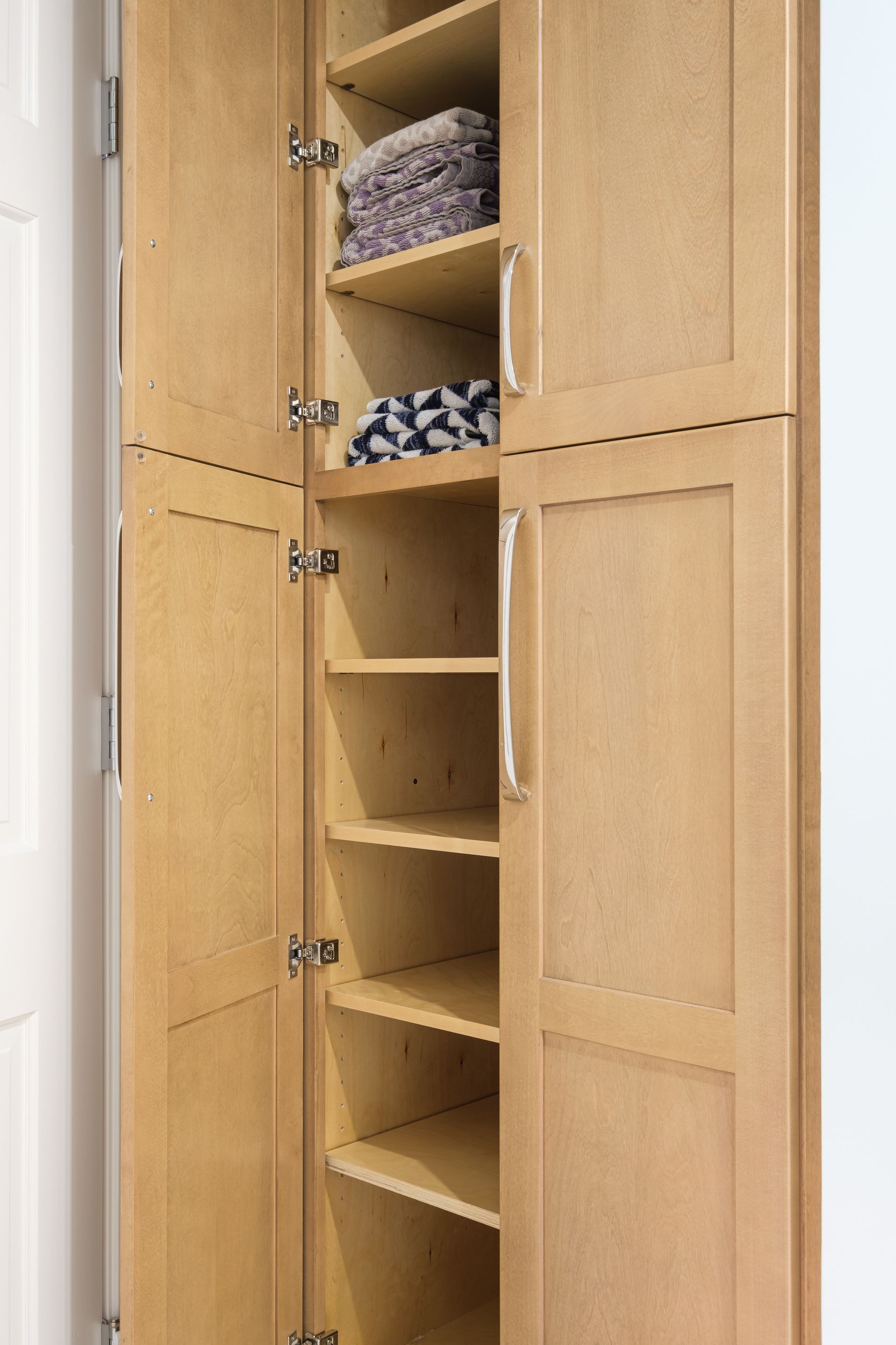 A wooden cabinet with the doors open and shelves filled with towels.