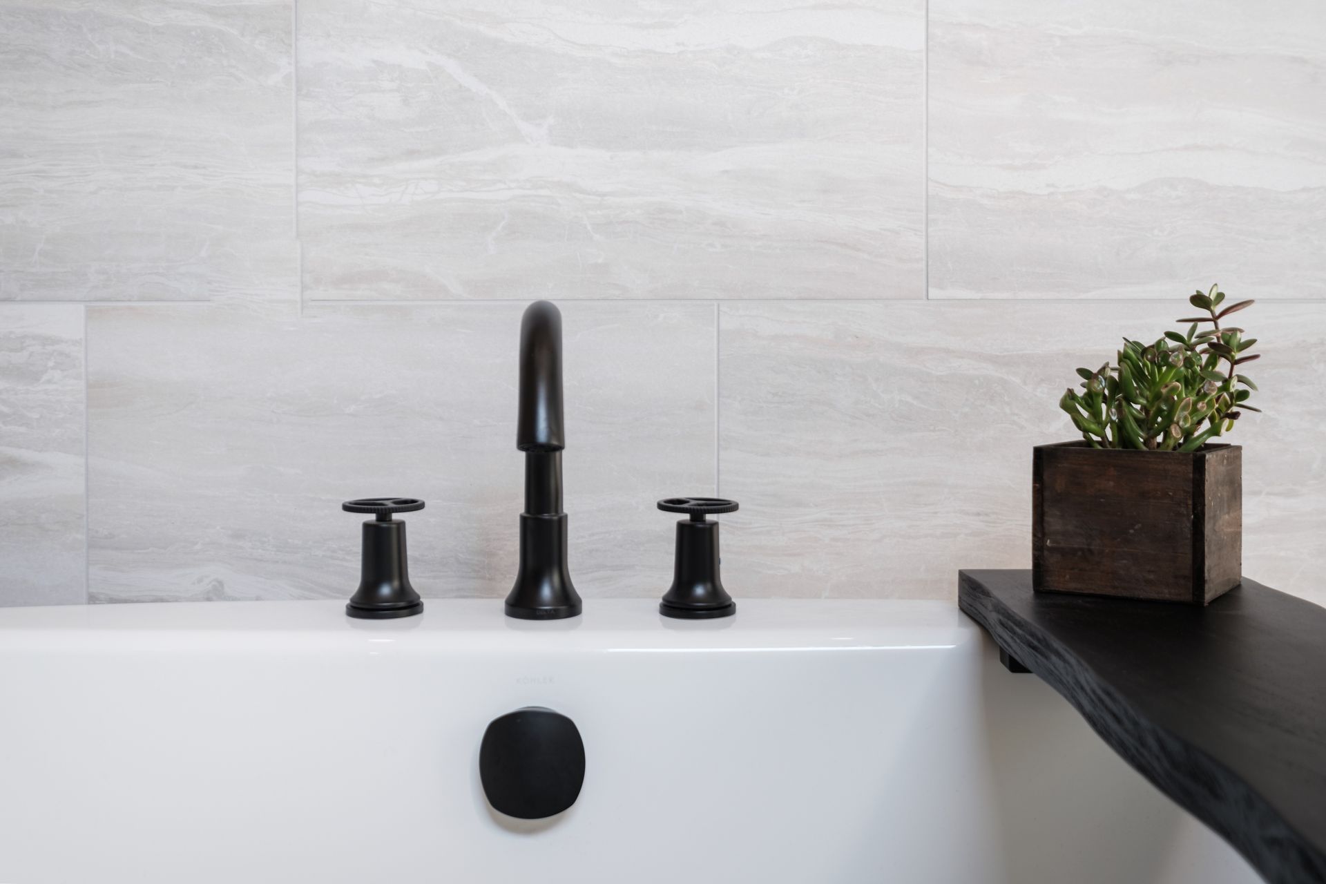 A white bathtub with black faucets and a potted plant on a shelf.