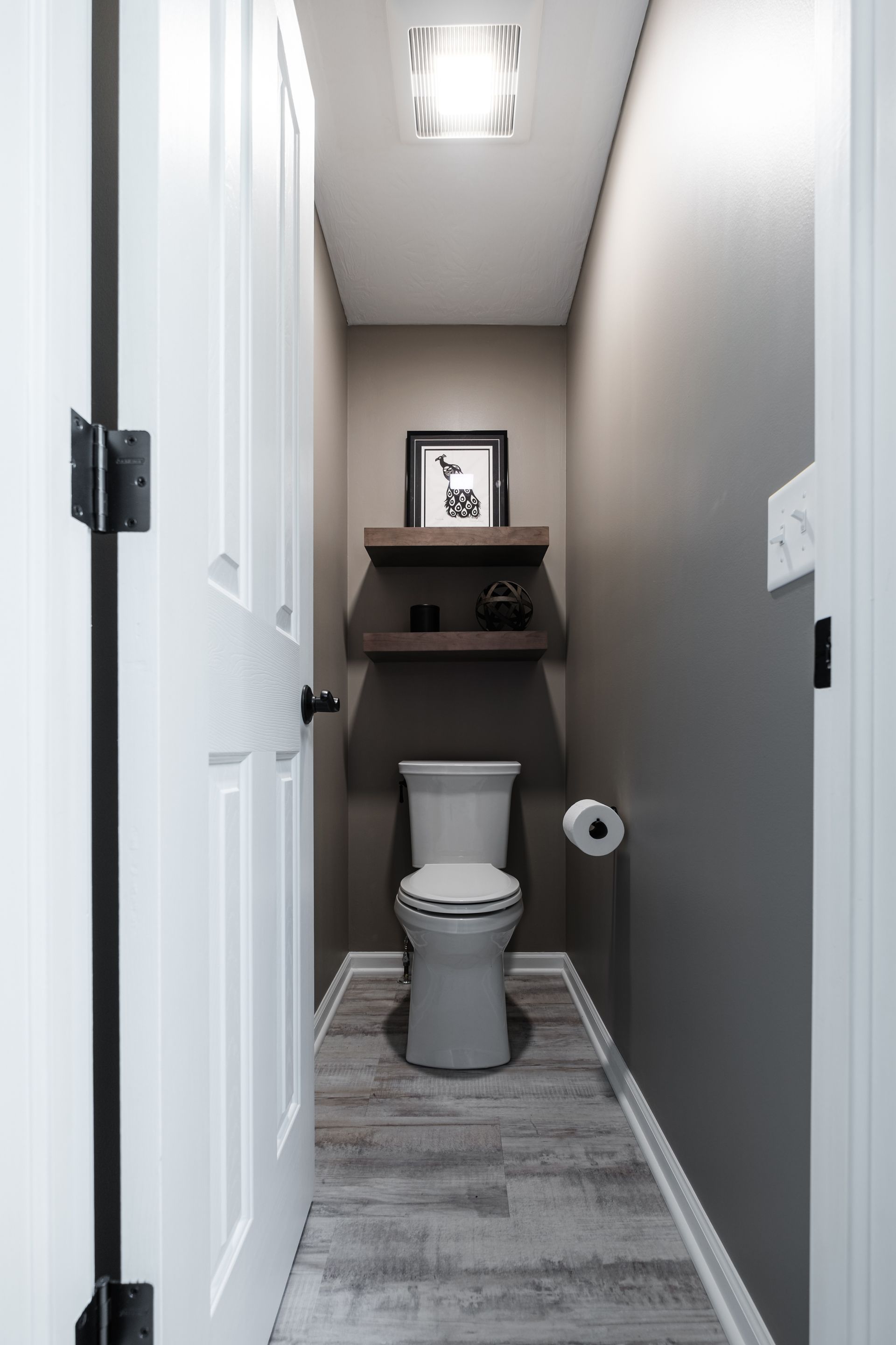 A narrow bathroom with a toilet , paper towel and a picture on the wall.