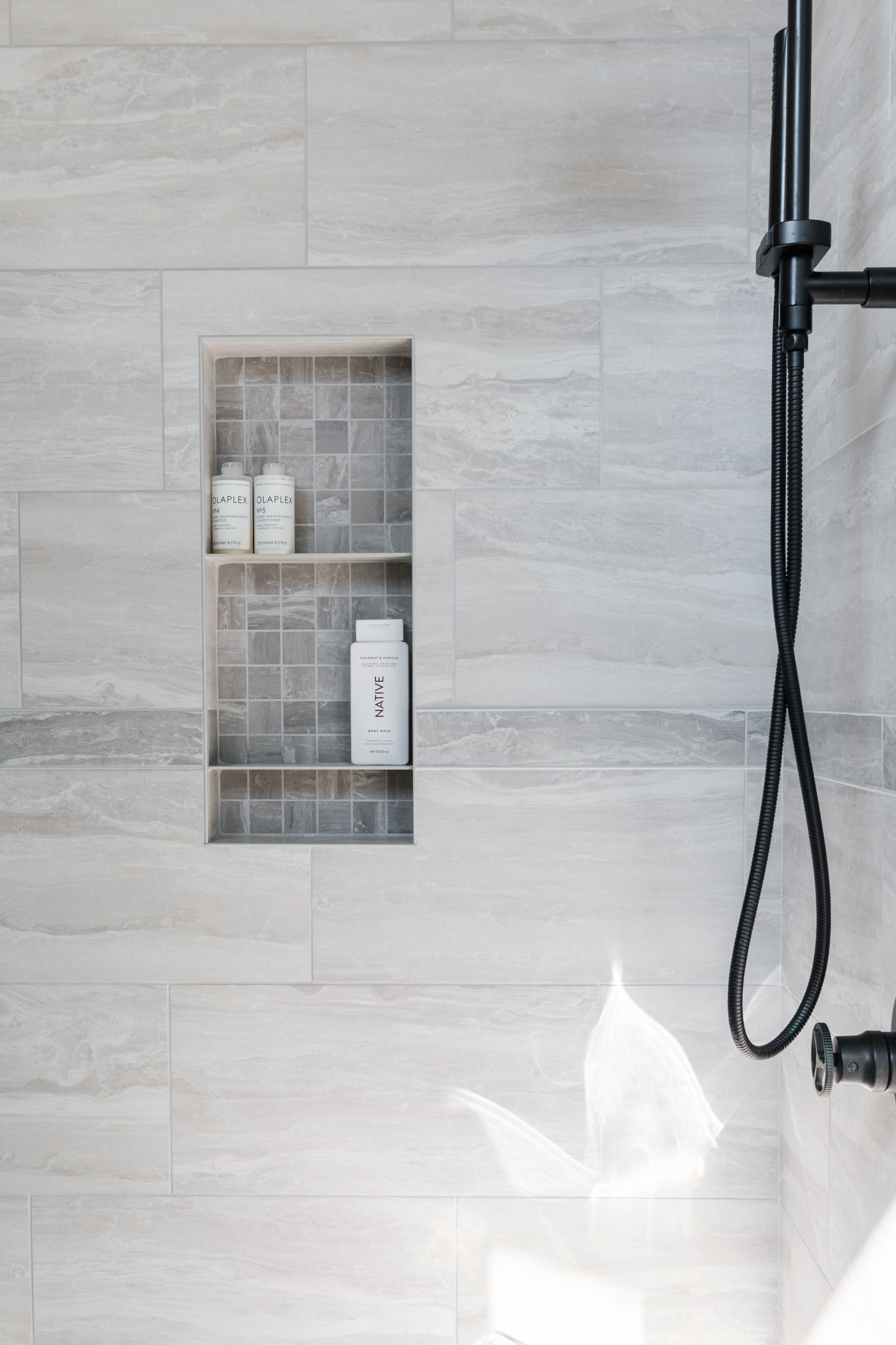 A shower with a built in shelf and a black shower head.