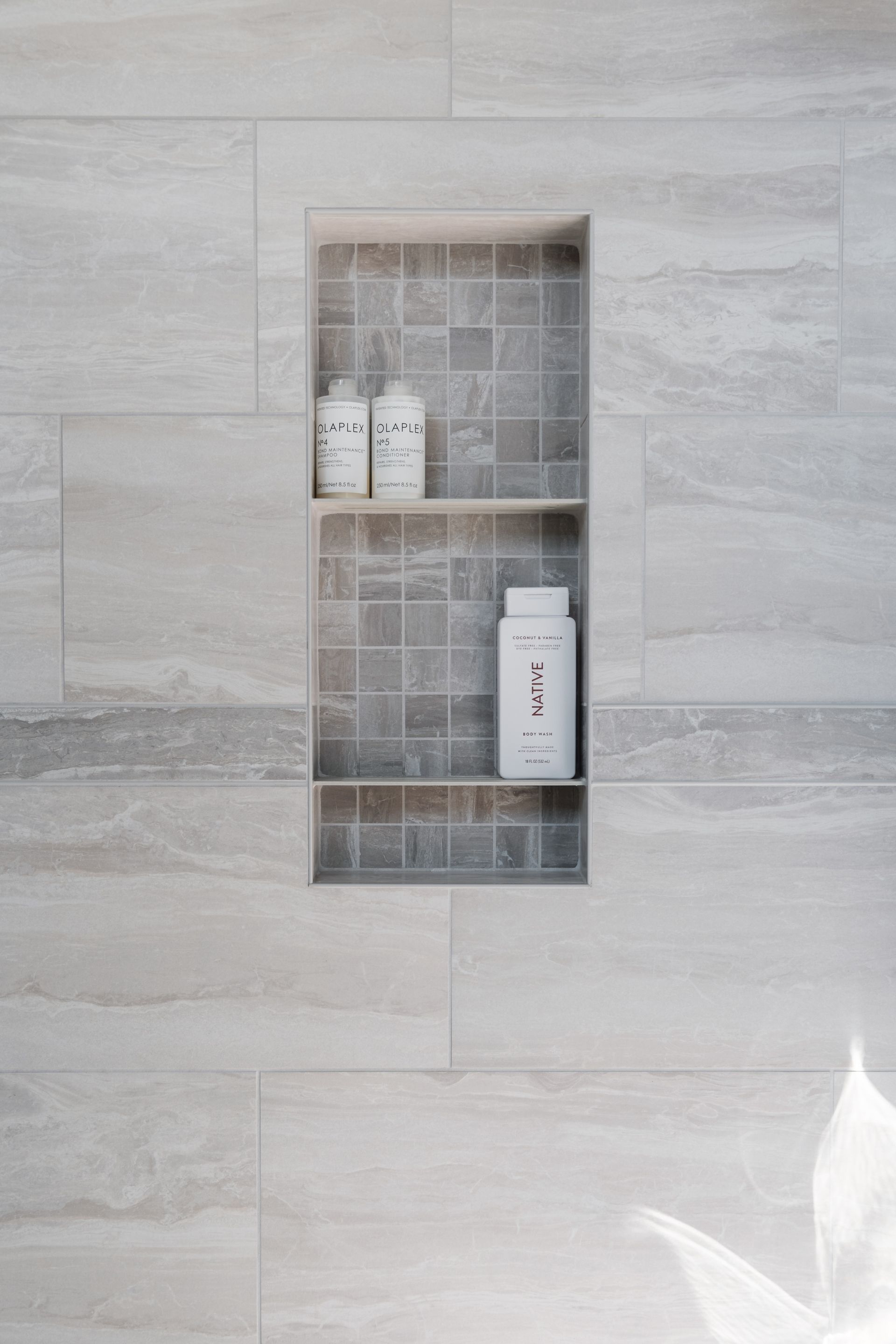 There is a shelf in the shower with bottles on it.