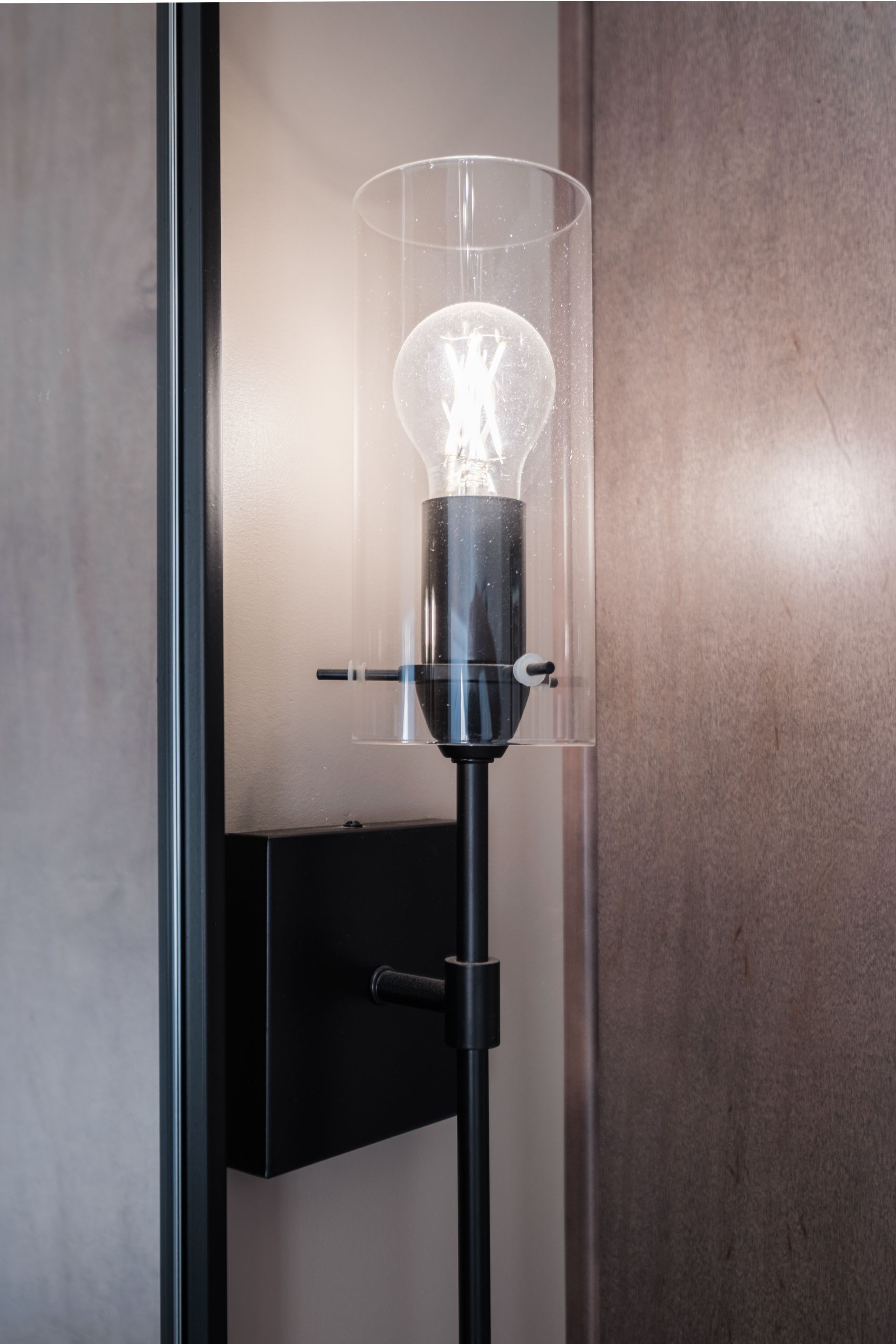 A lamp with a clear glass shade is hanging on a wall.