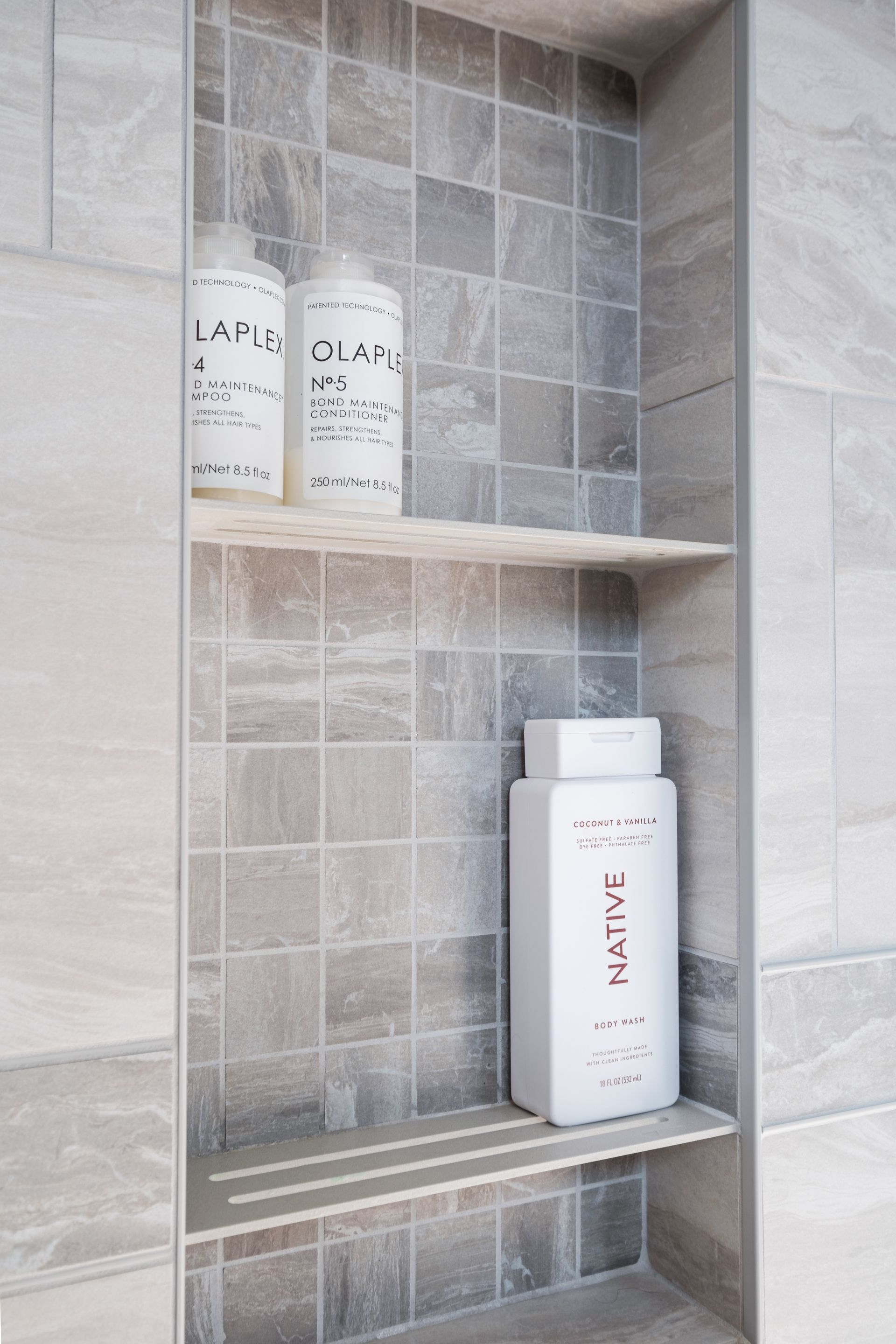 A bathroom shelf with bottles of shampoo and conditioner on it.