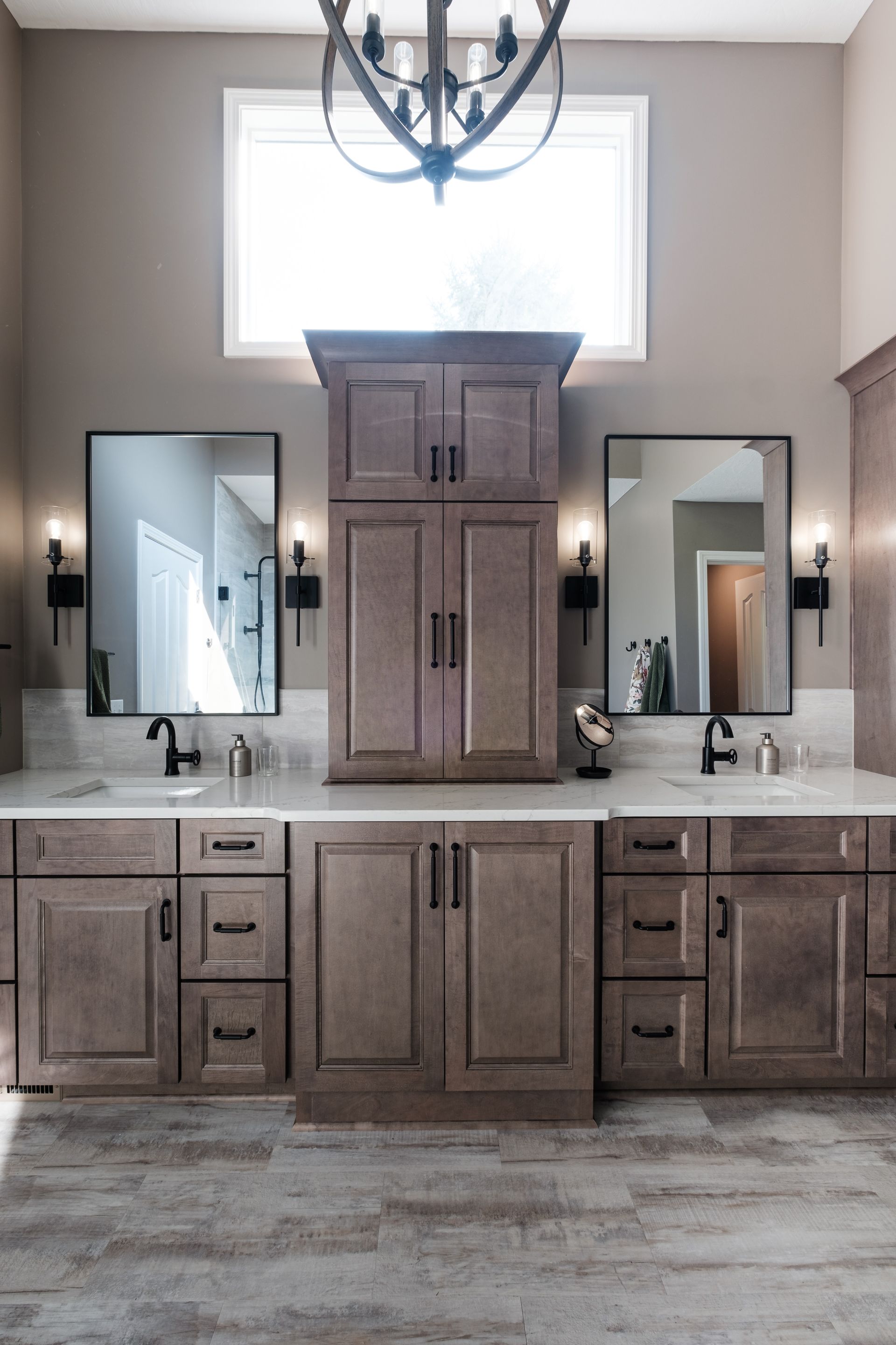 A bathroom with two sinks , two mirrors and a chandelier.