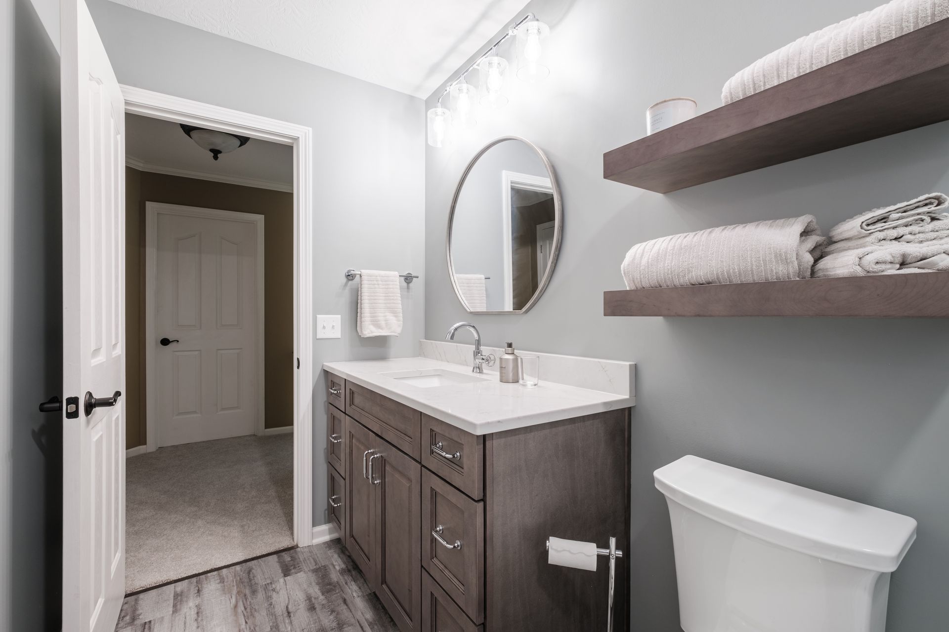 A bathroom with a sink , toilet , mirror and shelves.