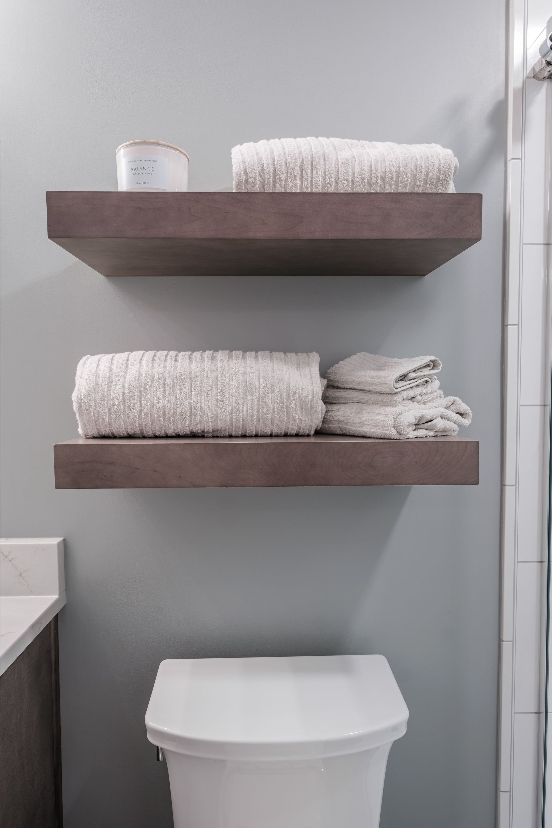 A bathroom with three shelves filled with towels and a toilet.