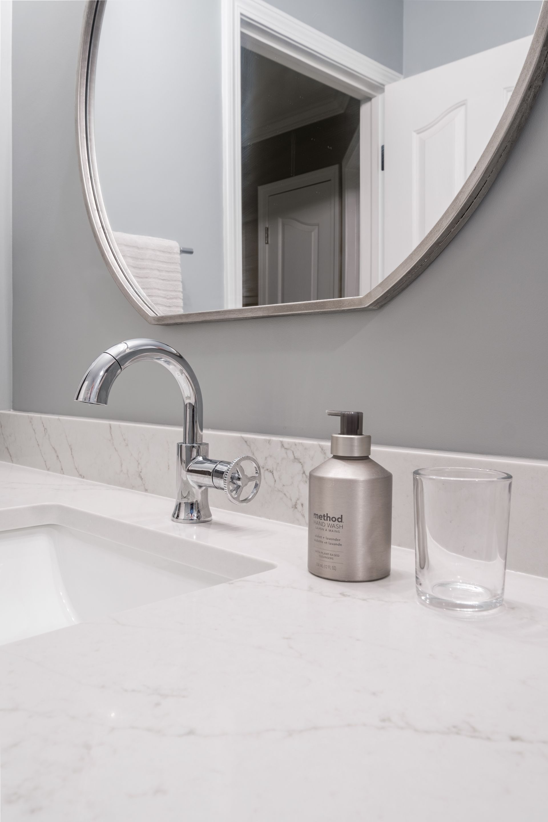 A bathroom sink with a round mirror and a soap dispenser on the counter.