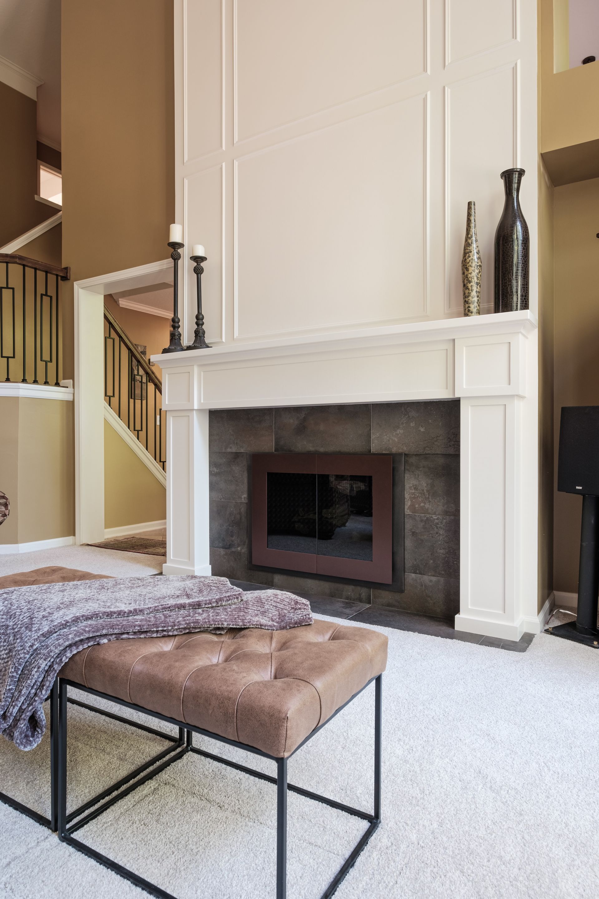 A living room with a fireplace , ottoman , coffee table and stairs.