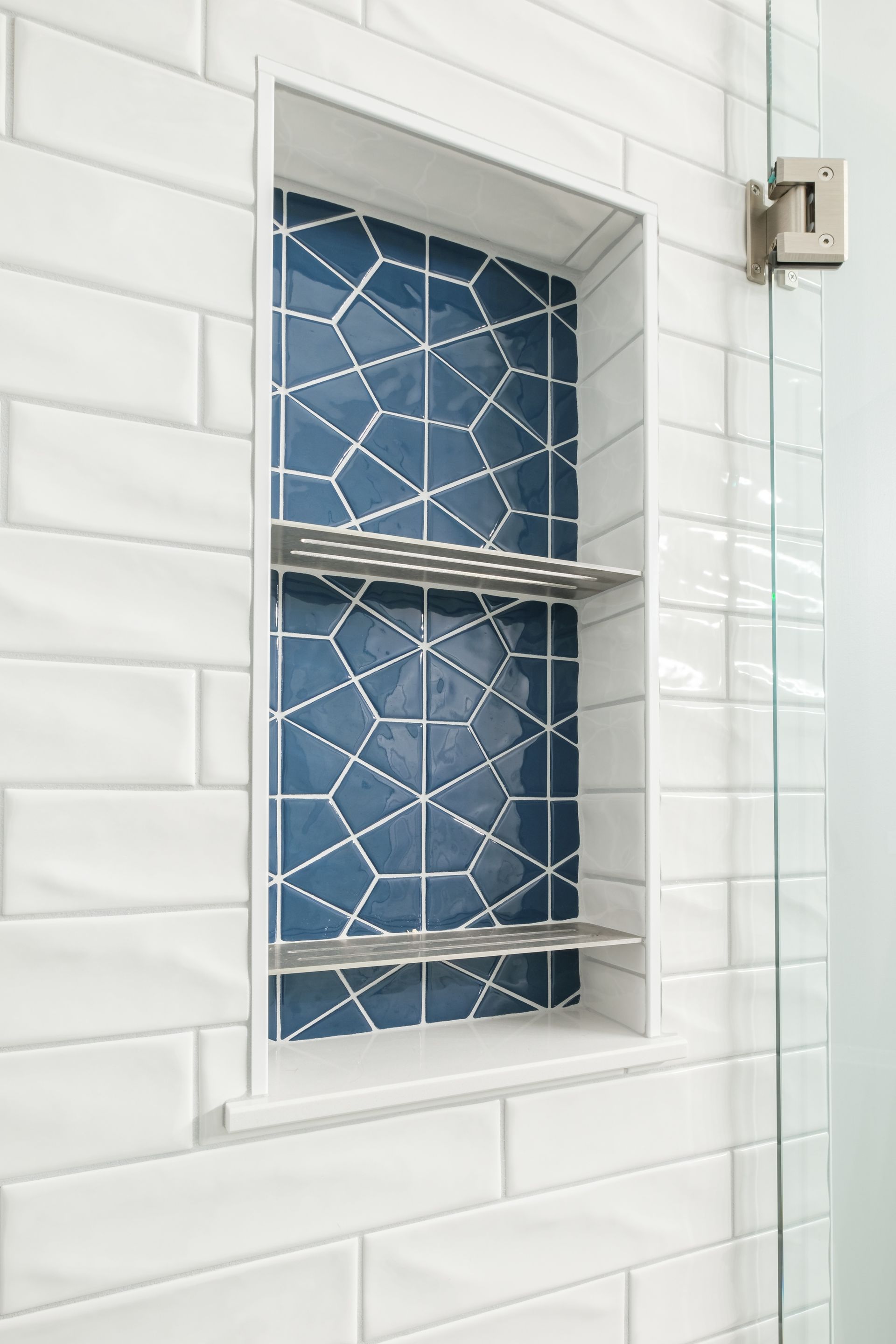 A shower niche with blue tiles and a shelf in a bathroom.