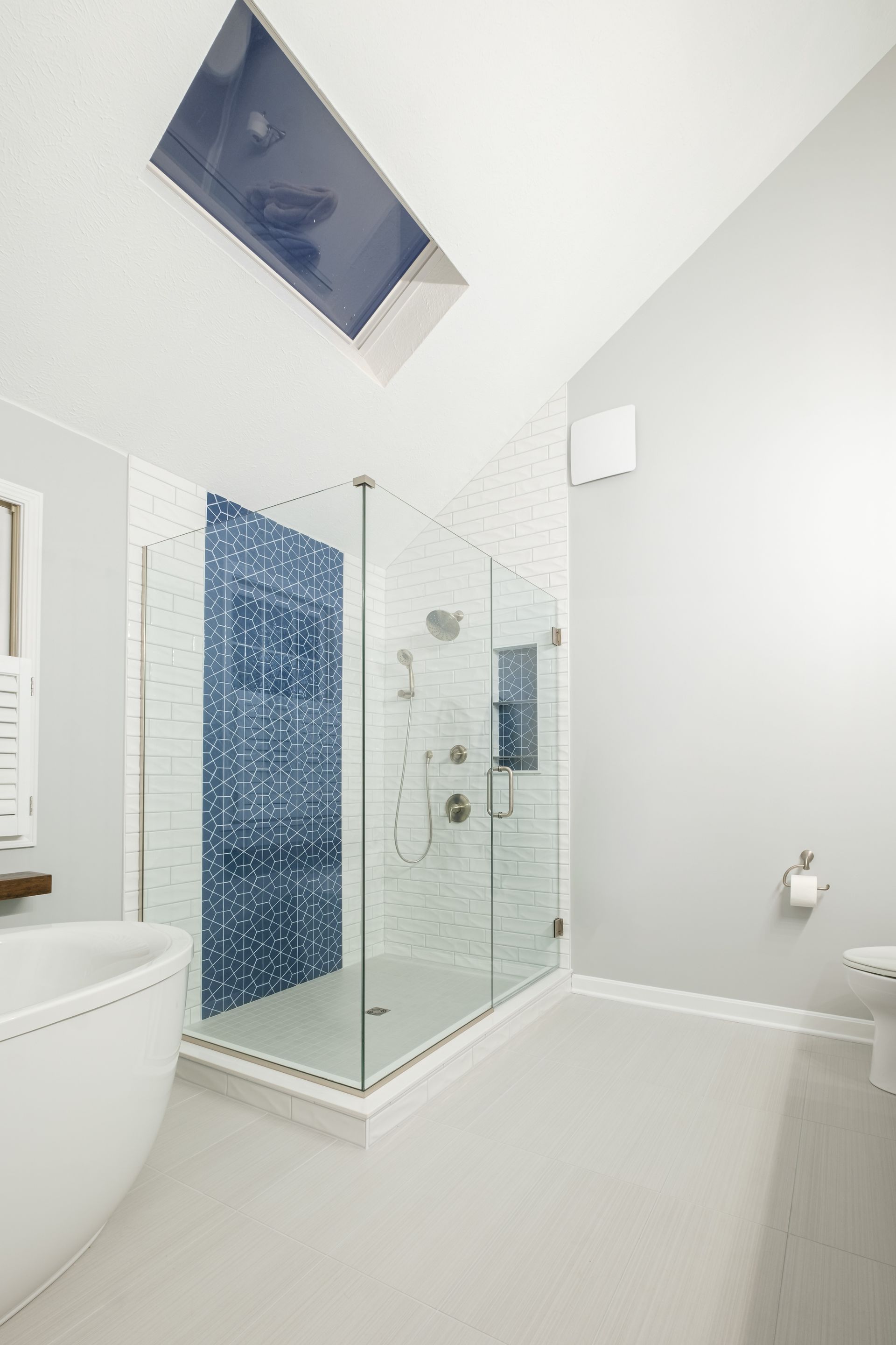 A bathroom with a walk in shower , tub and skylight.