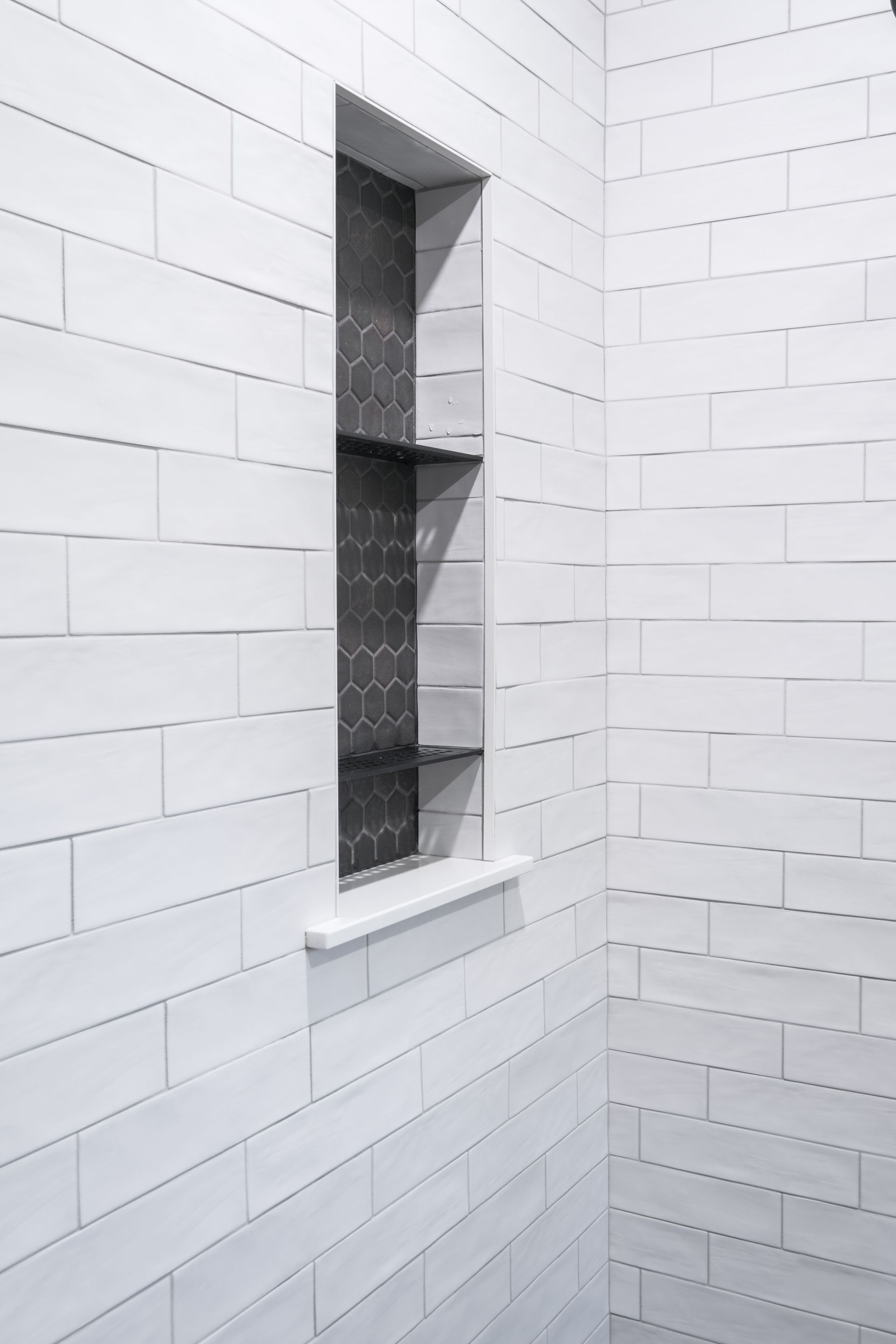 A shower with white tiles and a shelf in the wall.