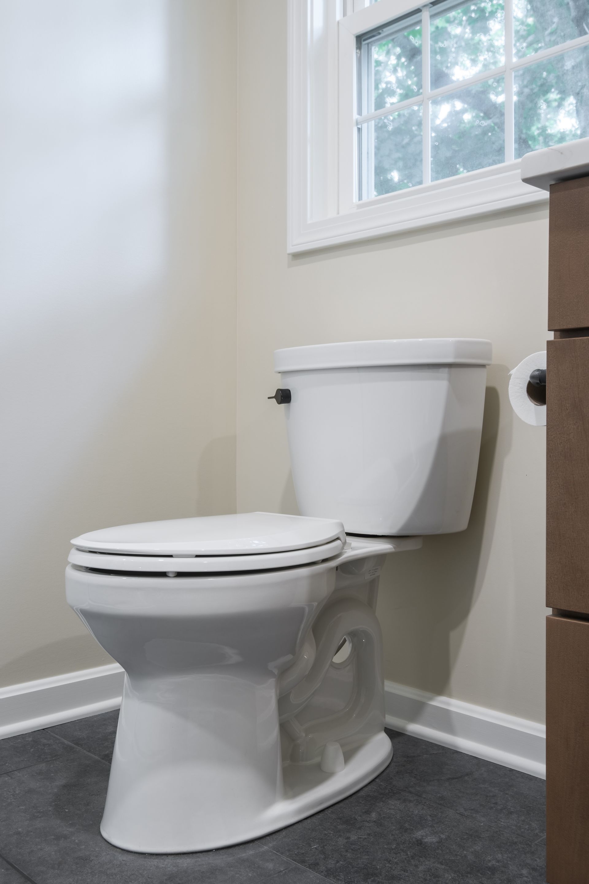 A white toilet is sitting in a bathroom next to a window.