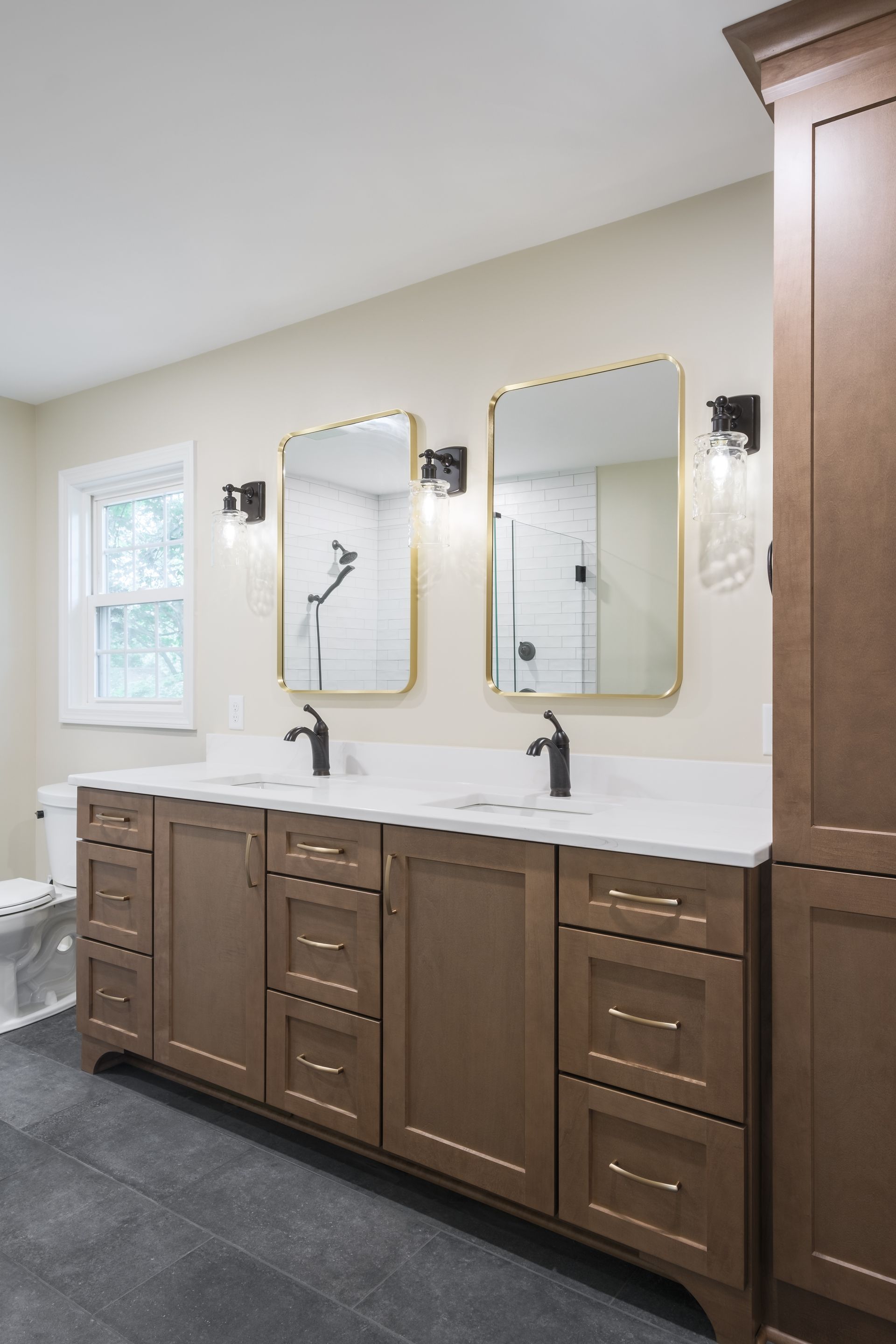 A bathroom with two sinks , two mirrors and a toilet.