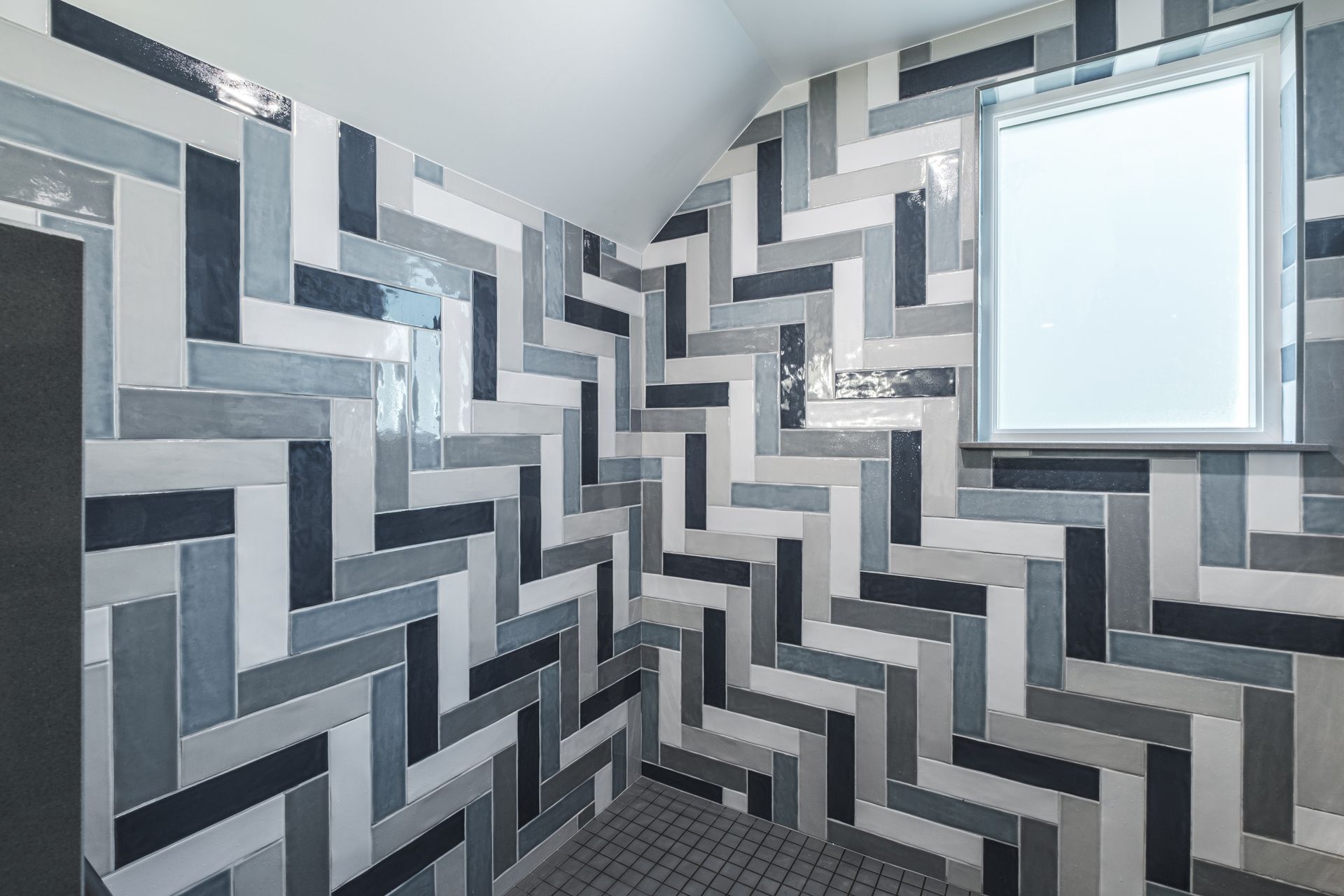 Bathroom with blue, gray, and white herringbone tile walls, small window, and dark shower floor.